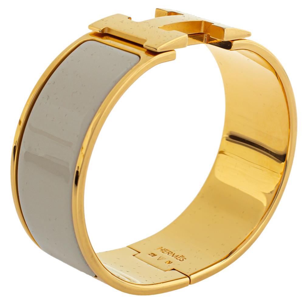 This elegant 'Clic Clac H' bracelet from the house of Hermes is designed in a wide silhouette. It features a gold-plated body with cream enamel on it and the iconic 'H' logo swivel at the centre. Wear it with your favourite watch or as an