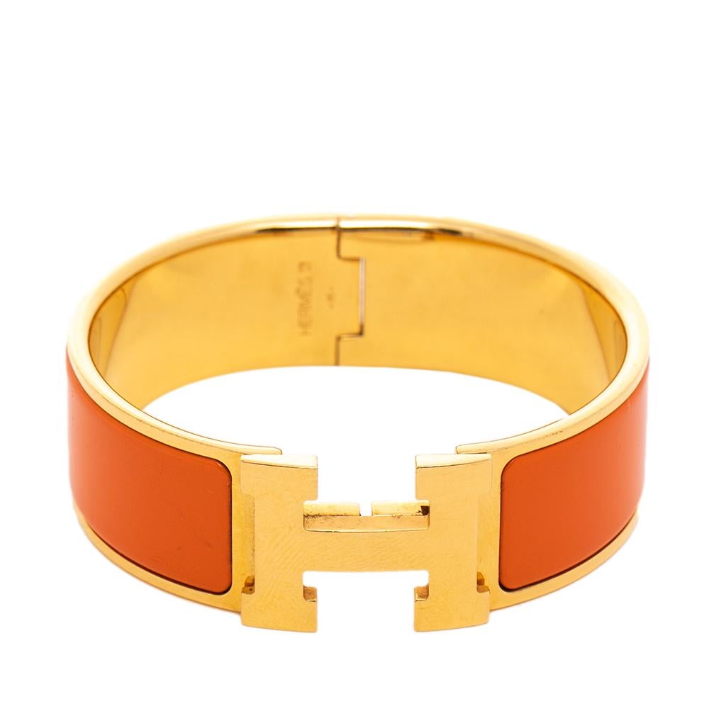 This elegant 'Clic Clac H' bracelet from the house of Hermès is designed in a wide silhouette. It features a gold-plated body with orange enamel on it and the iconic 'H' logo swivel at the center. Wear it with your favorite watch or as a solo