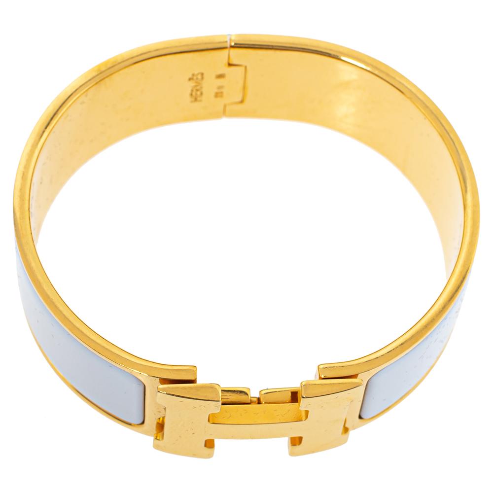 This simply elegant 'Clic Clac H' bracelet from the house of Hermes is designed in a wide silhouette. It features a gold-plated body with white enamel on it and the iconic 'H' logo swivel at the centre. Wear it with your favourite watch or as an