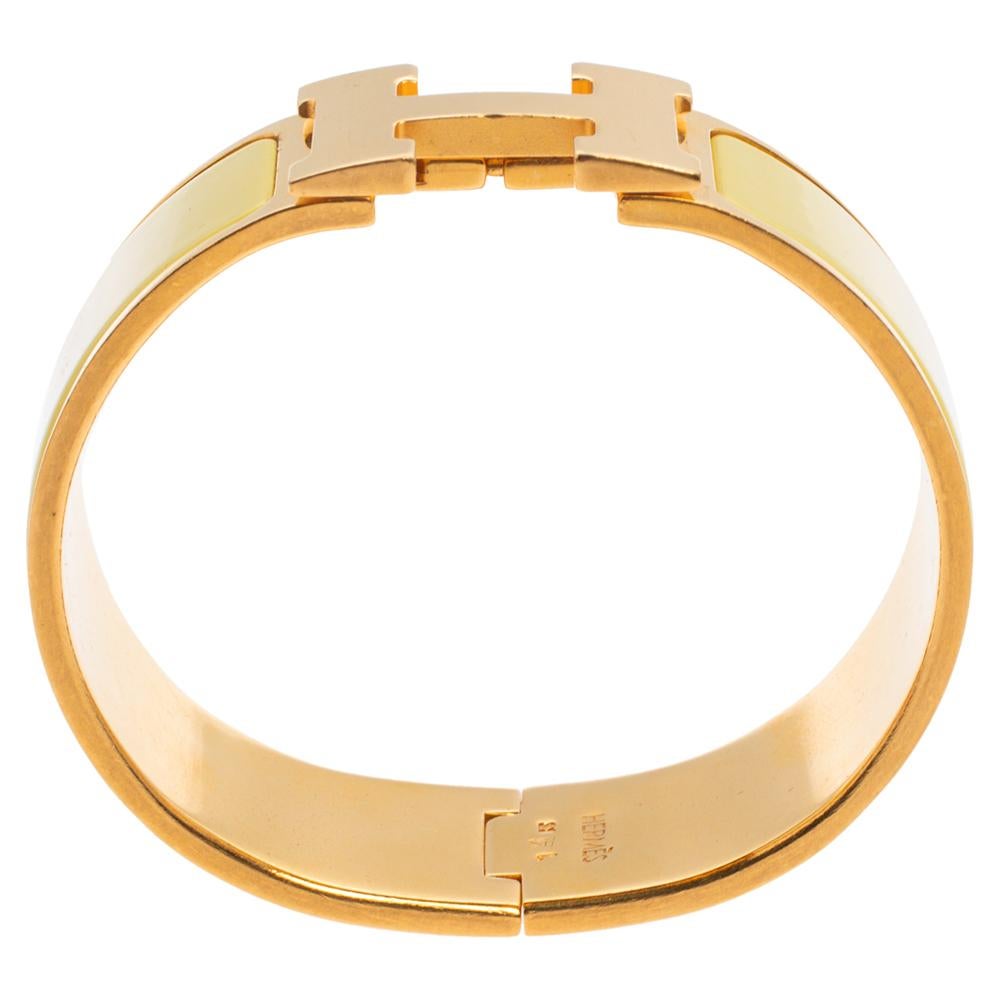 This elegant 'Clic Clac H' bracelet from the house of Hermes is designed in a wide silhouette. It features a gold-plated body with yellow enamel on it and the iconic 'H' logo swivel at the center. Wear it with your favorite watch or as a solo