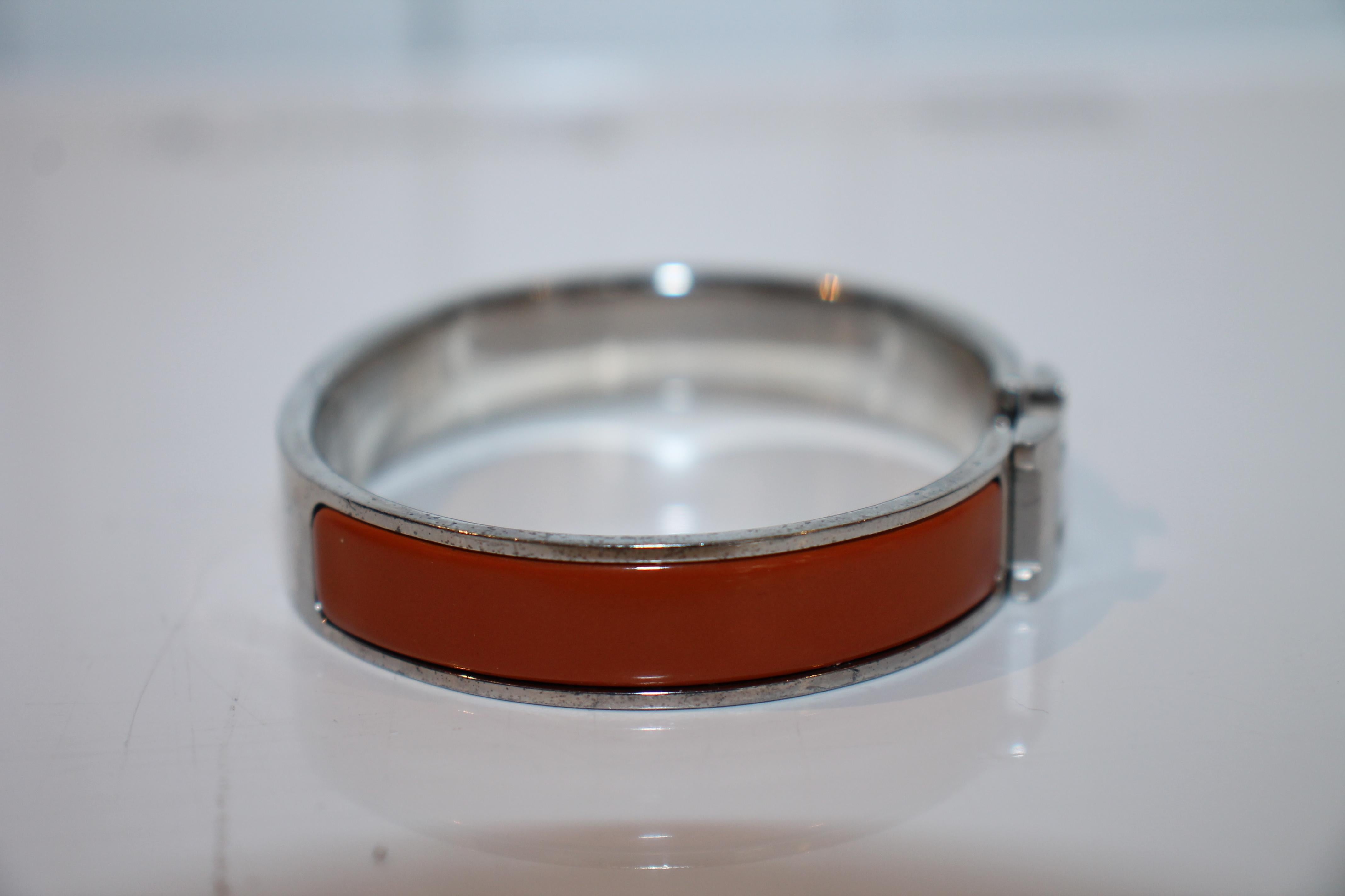 Palladium-plated Hermès Clic Clac H bracelet featuring brownish orange enamel inlays and hinged clip closure. (Size: 1)