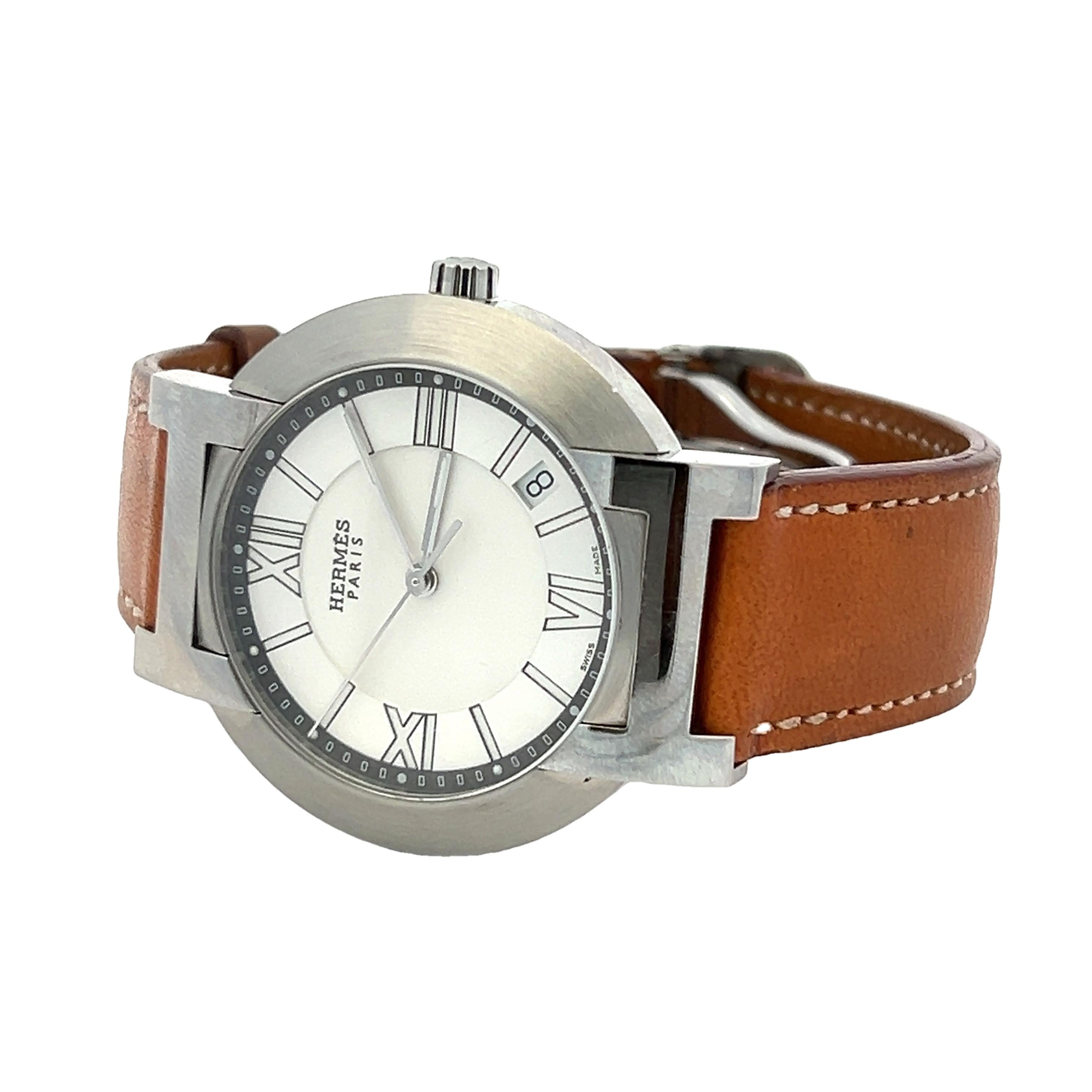 Timeless and impeccably crafted, this Hermès wristwatch blends the house’s equestrian heritage with sleek, modern lines. The brushed stainless steel case features bold architectural lugs and a minimalist round dial framed with elegant Roman