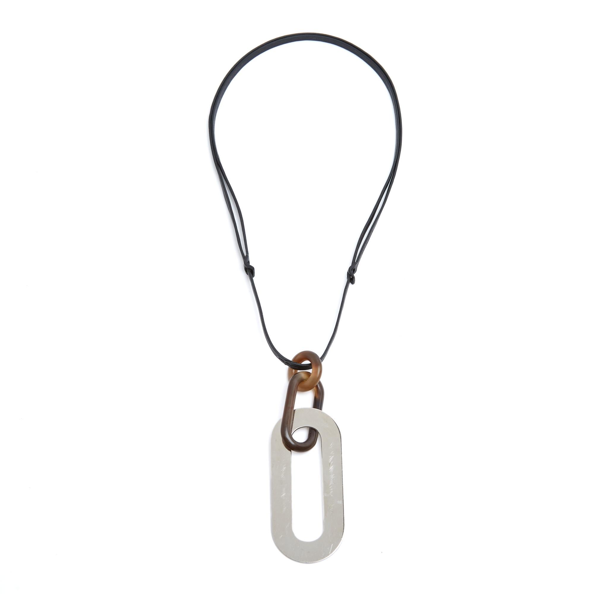 Collana Hermès modello Pigment composta da un lungo ciondolo a 3 anelli in acciaio o metallo argentato (palladio) e corno naturale, montato su un cinturino in pelle regolabile. Lunghezza totale della collana (massima, escluso il ciondolo) 44 cm,