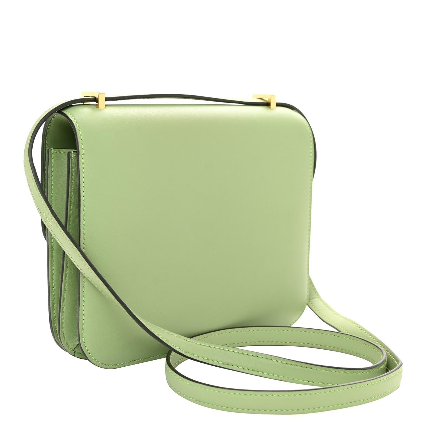 This is an authentic HERMES Swift Constance 18 in Vert Criquet. This is a chic small bag that is finely crafted of luxurious calfskin leather in pale green. The bag features a leather crossbody shoulder strap, a front flap, and a polished gold