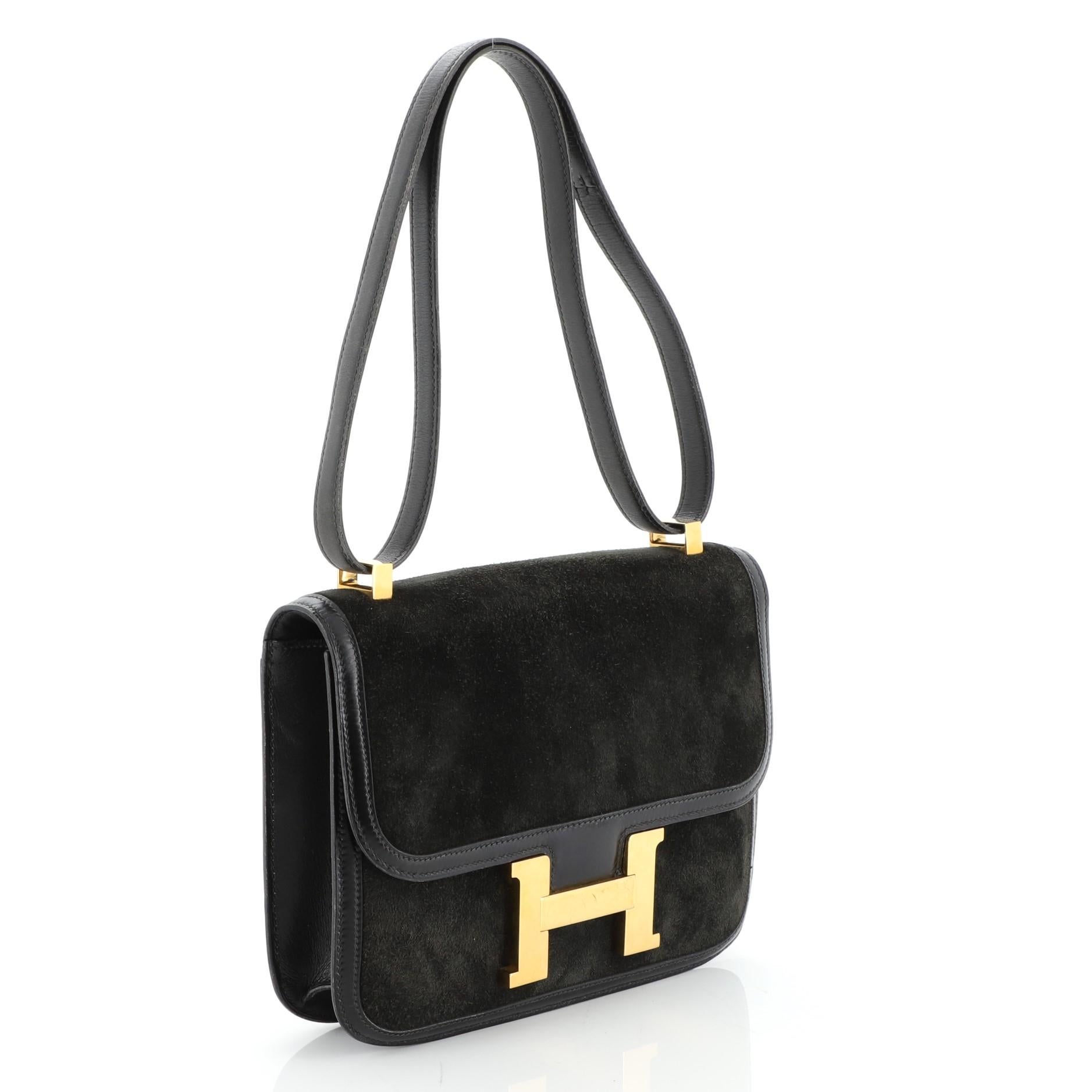 This Hermes Constance Bag Doblis Suede with Box Calf 24, crafted from Noir black Veau Doblis and Box Calf leather, features a long leather strap and gold hardware. Its push-lock closure opens to a Noir black Agneau leather interior divided into two