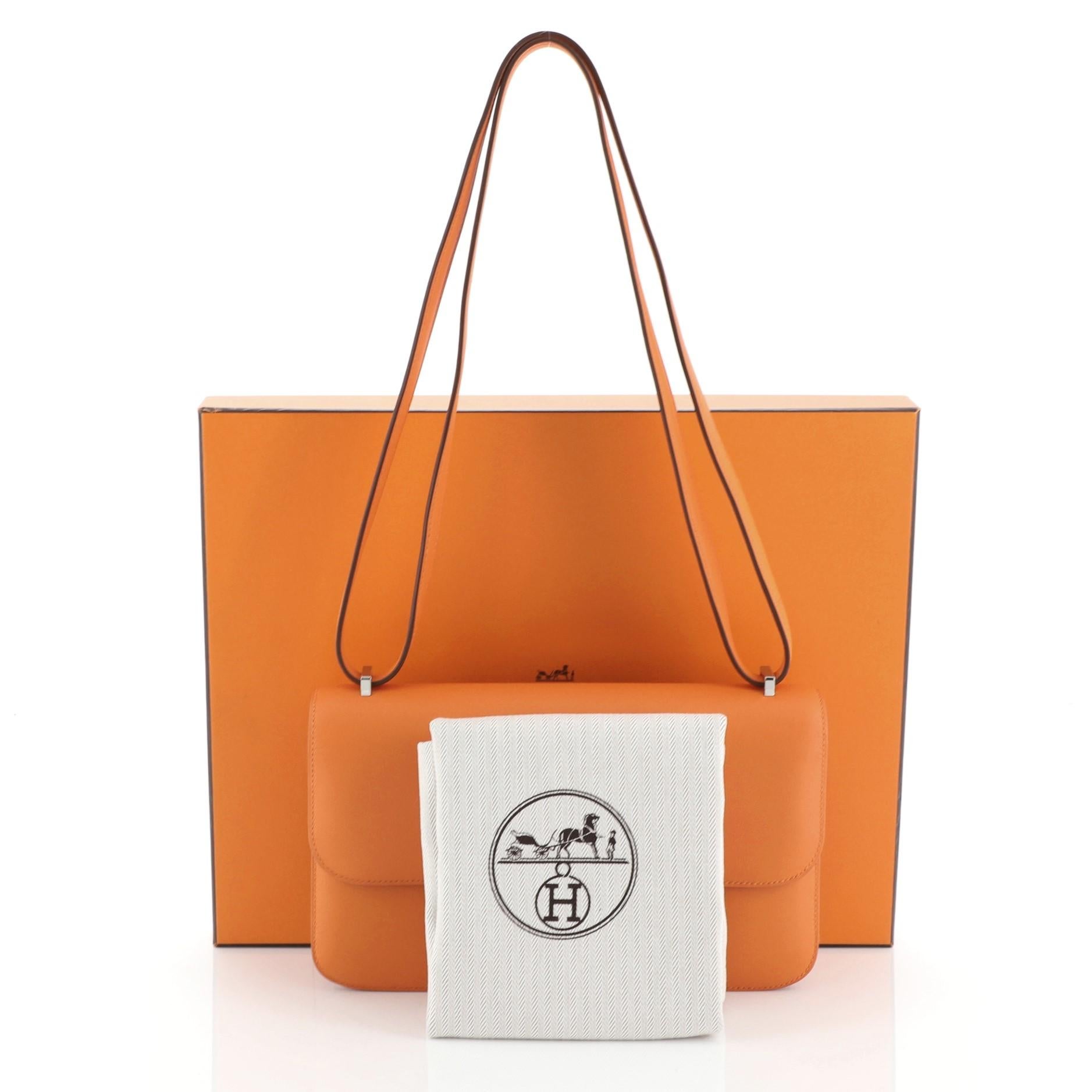 This Hermes Constance Elan Bag Swift 25, crafted from Orange H Swift leather, features a long leather strap and palladium hardware. Its push-lock closure opens to an Orange H Swift leather interior divided into two compartments with zip and slip