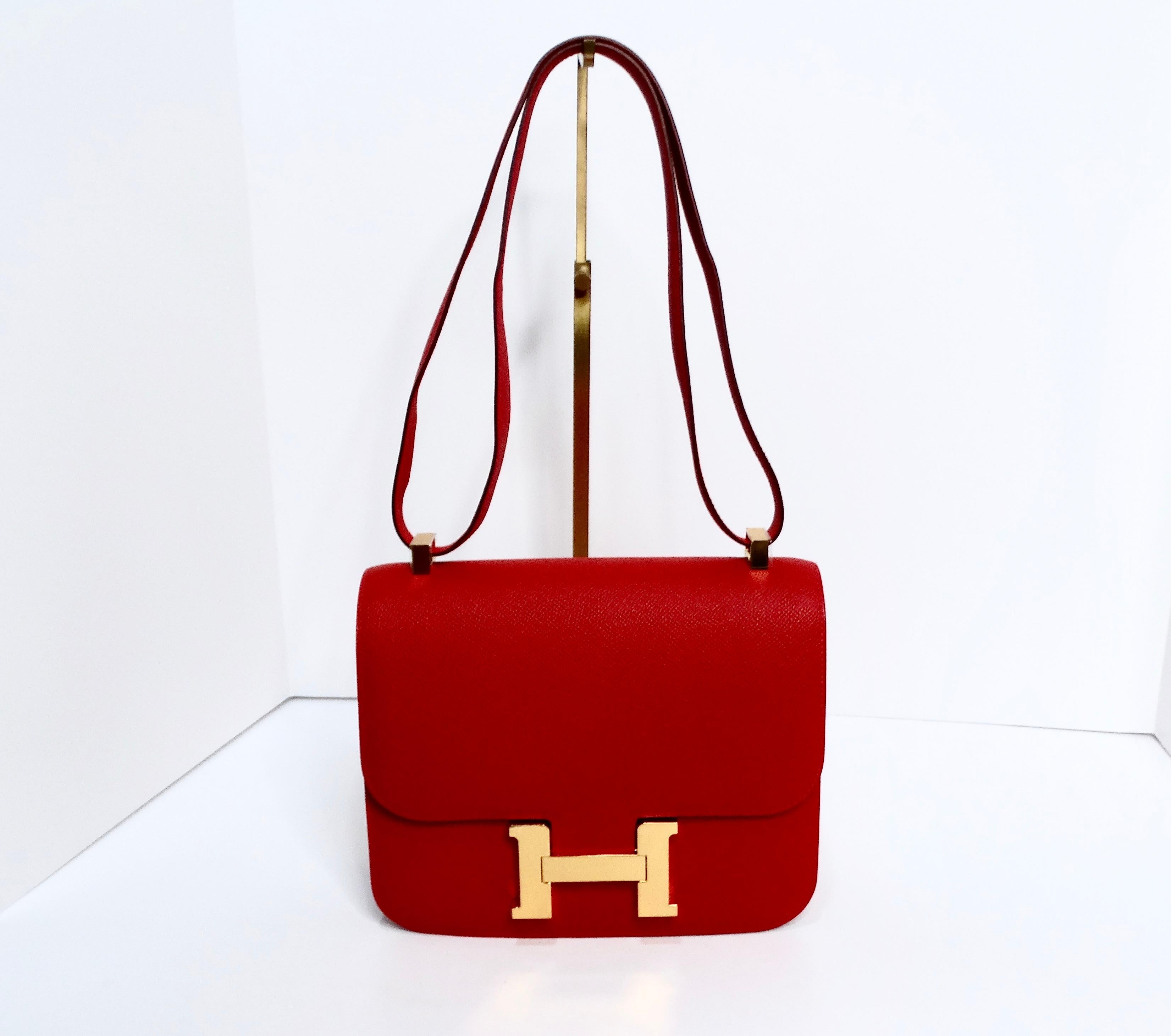 The Hermès Constance in Epsom Rouge Casque 24 with gold hardware is a stunning example of high fashion craftsmanship. This iconic 24cm bag is crafted from luxurious Epsom leather, known for its durability and textured finish, making it a practical