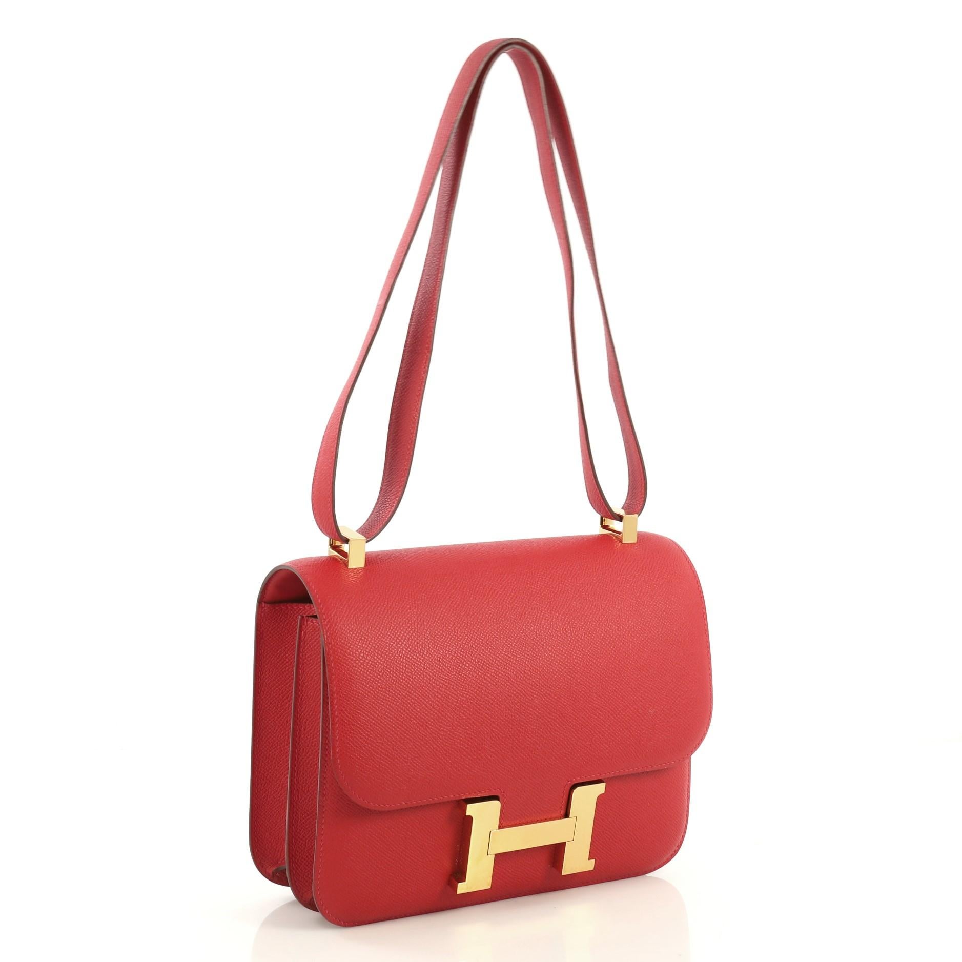This Hermes Constance Handbag Epsom 24, crafted from Vermillion red Epsom leather, features a long leather strap and gold hardware. Its push-lock closure opens to a Vermillion red Agneau leather interior divided into two compartments with zip and