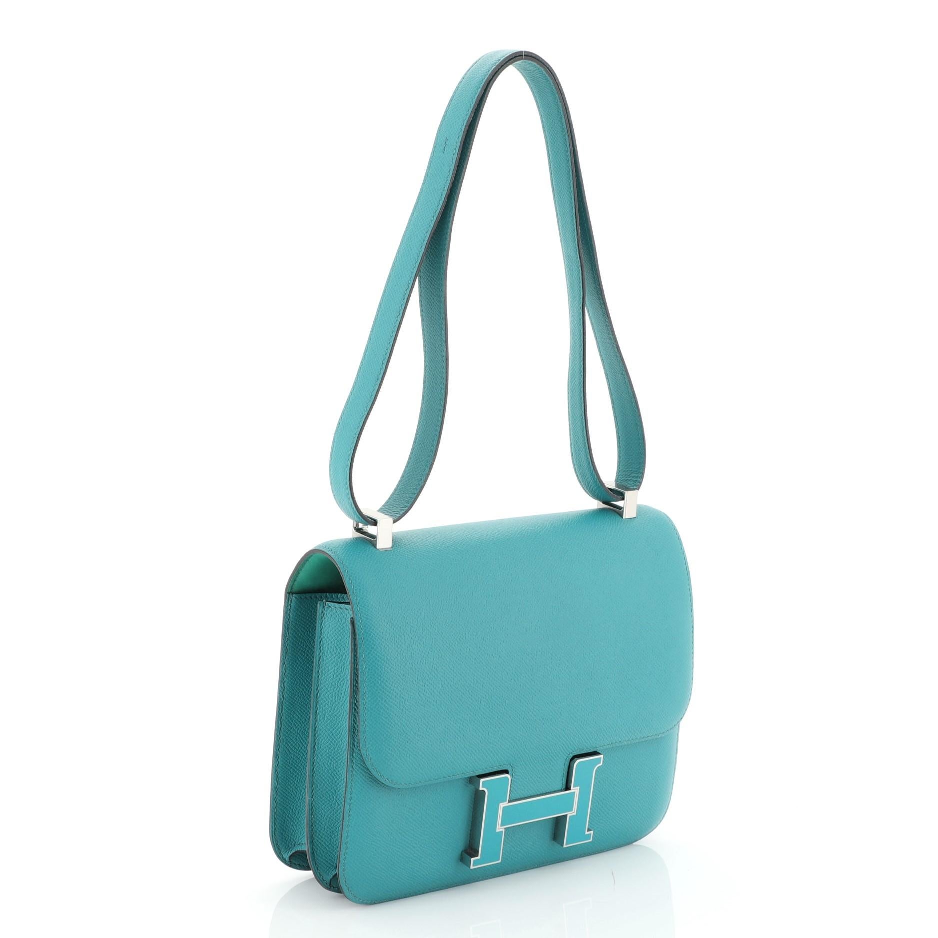 This Hermes Constance Handbag Epsom 24, crafted from Bleu Paon blue Epsom leather, features a long leather strap and palladium hardware. Its push-lock closure opens to a Menthe green Agneau leather interior divided into two compartments with zip and