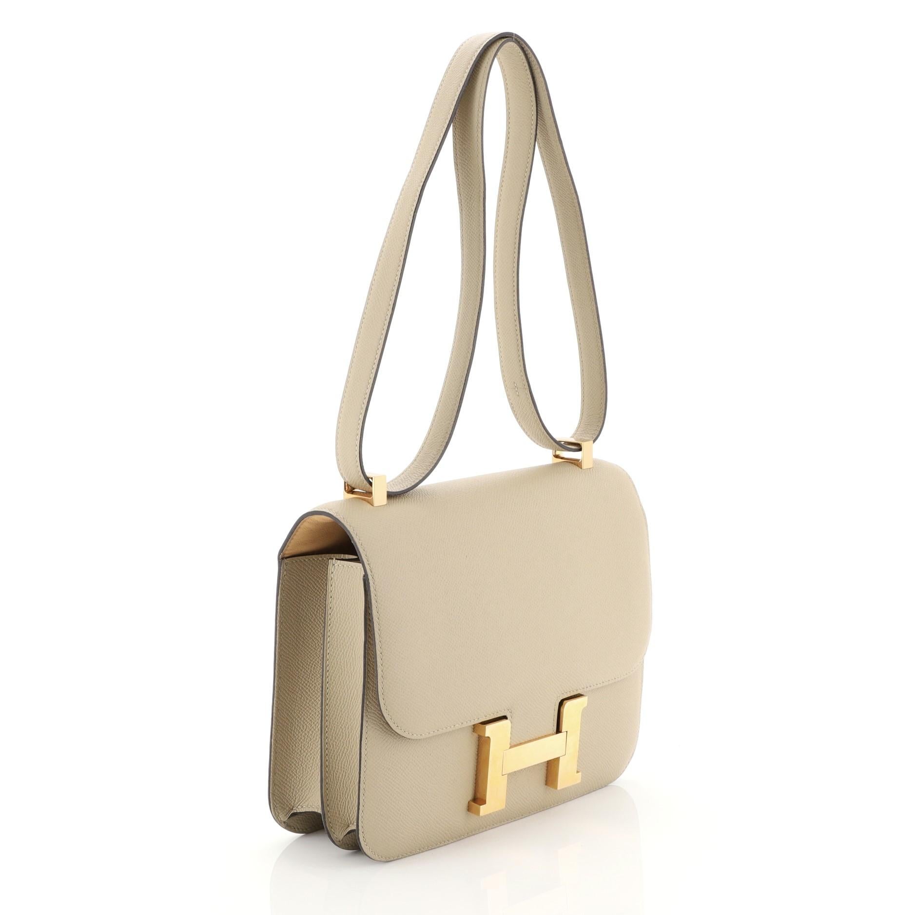 This Hermes Constance Handbag Verso Epsom 24, crafted from Trench neutral Epsom leather, features a long leather strap and gold hardware. Its push-lock closure opens to a Natural Sable Agneau leather interior divided into two compartments with zip