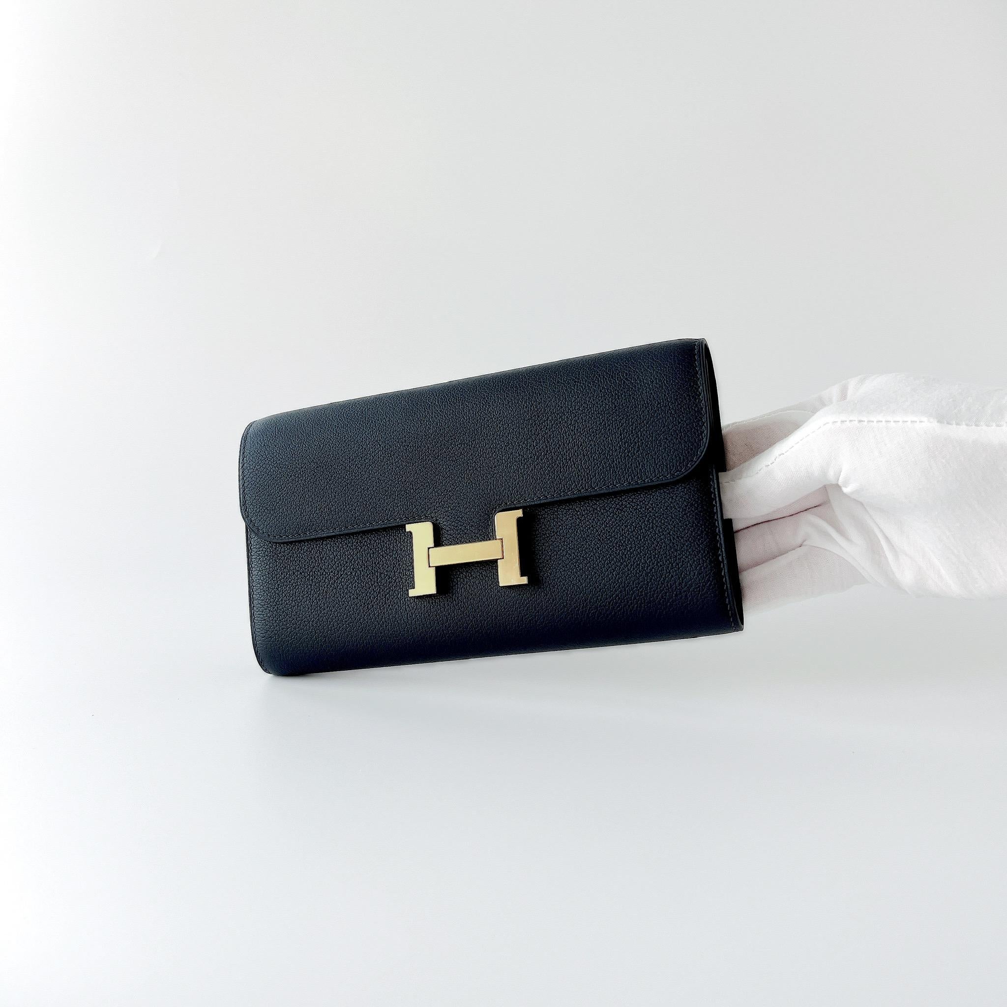 A beautiful Constance Long To Go Wallet In Bleu Nuit And Gold Hardware. This wallet has a strap making it perfect as a small bag. Inside has 4 credit card slots, 2 pockets, 1 zipped change purse and an exterior pocket. 

Brand: Hermès

Colour: Navy