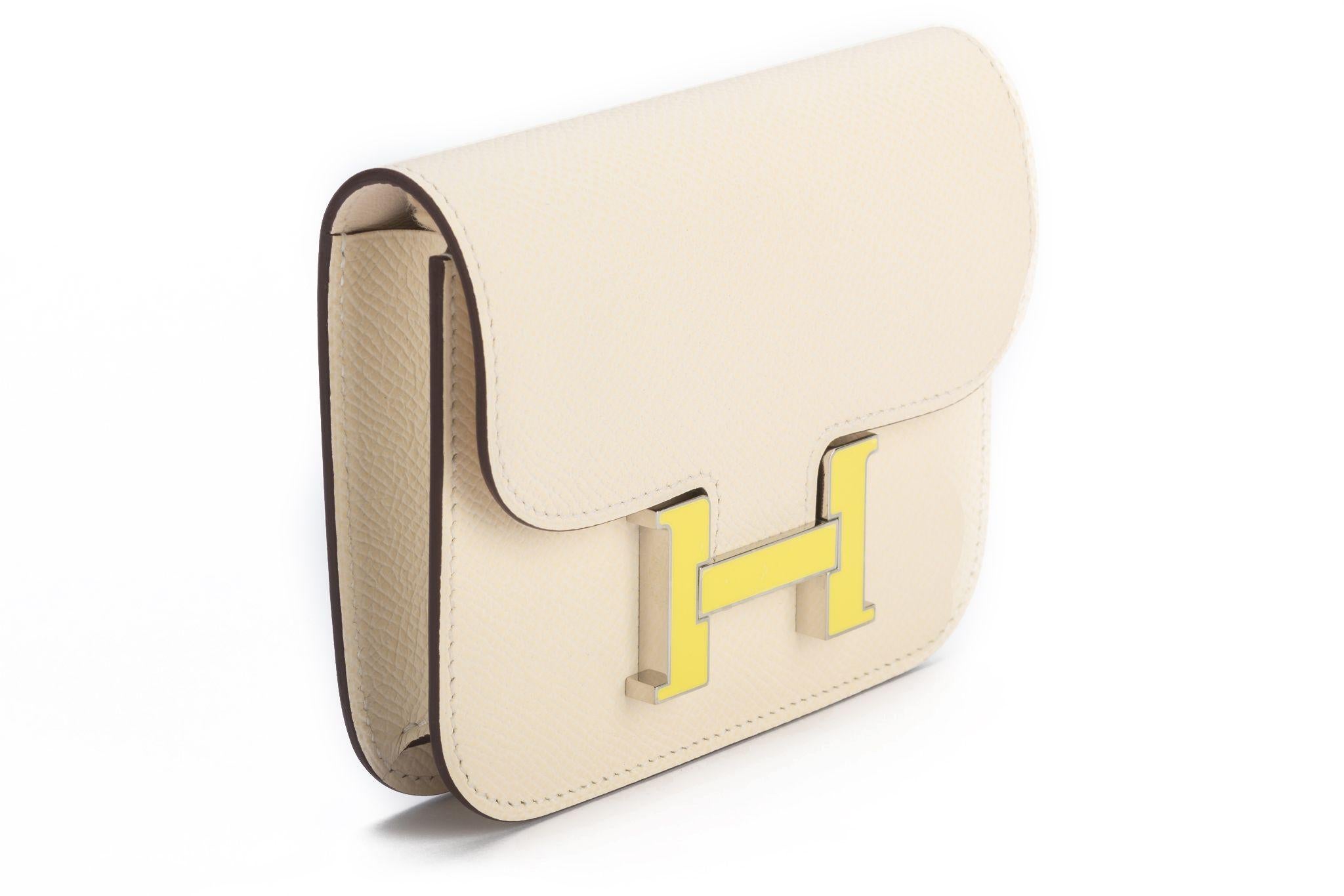 Portefeuille mince Hermès en veau craie Epsom avec porte-monnaie amovible zippé, 2 emplacements pour cartes de crédit, passant de ceinture et fermeture en émail jaune et plaqué palladium. La pièce est dans la couleur Craie Off White de la maison.