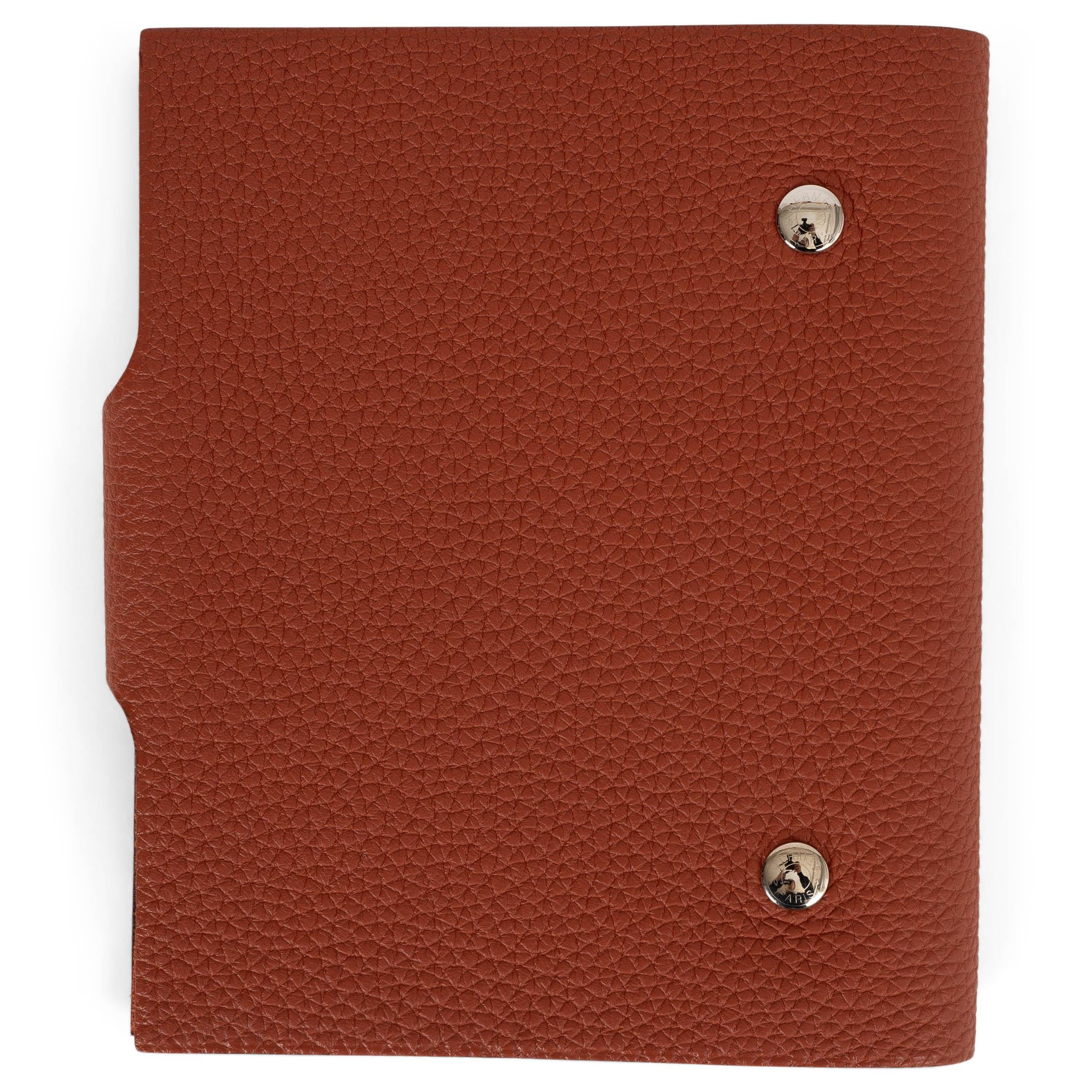 This 100% authentic Hermès Ulysse PM agenda cover in Cuivre (brick) Veau Togo leather is a refined blend of practicality and elegance. A limited edition piece, it features a subtle horse stamp on the front corner, adding a unique touch. Designed for