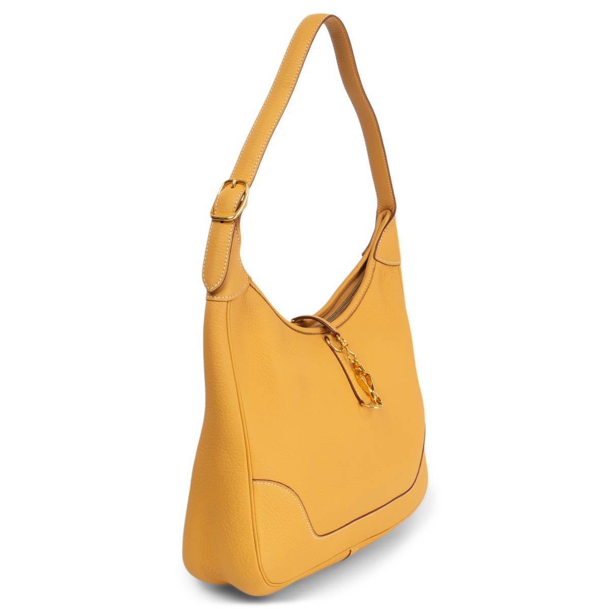100% authentic Hermès Trim 31 hobo in Curry yellow soft Taurillon Clemence leather featuring gold-tone hardware. Designed with adjustable shoulder handle, clasp opening with top zipper closure and gusseted sides. Unlined interior with a one slip