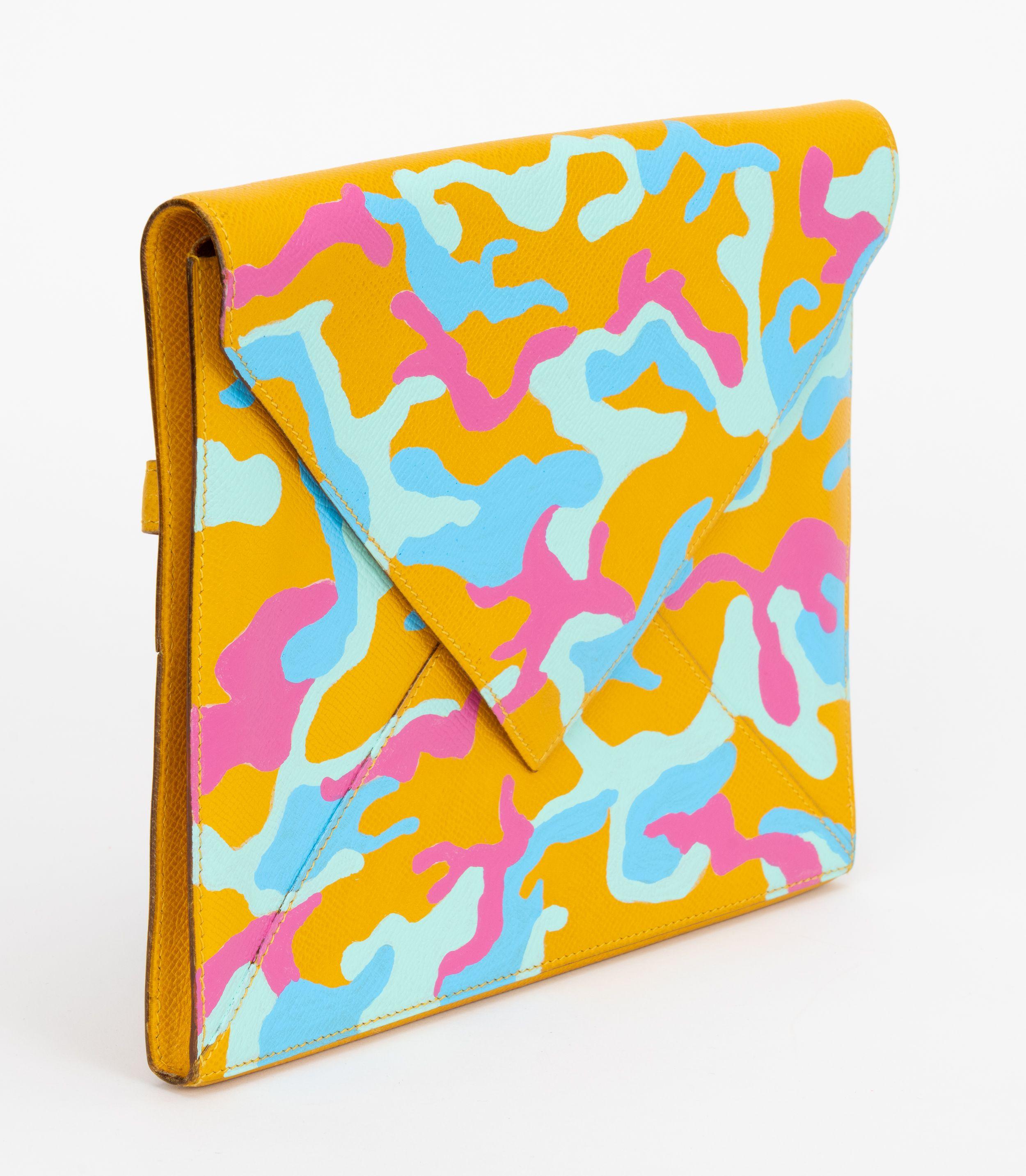 Pochette vintage Hermès jaune soleil peinte à la main par un artiste américain avec des couleurs pastel et un motif camouflage. Pièce unique en son genre, avec une sangle arrière inhabituelle pour maintenir la pochette. 
Timbre dateur T dans un