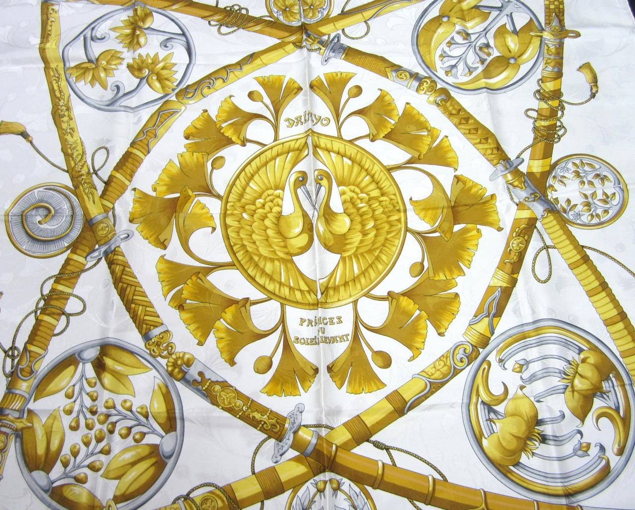 White background with gold, grays on this Hermes Silk Scarf Measures 34 in x 34 in. Never worn. Box included (box has a bit of wear at the corners) We have tons of silk scarves on our storefront Hermes, Gucci and Escada. Please be sure to check our