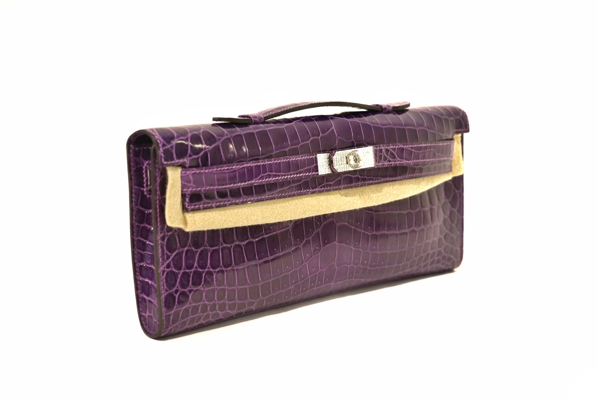 This authentic Hermès Diamond Amethyst Crocodile Kelly Cut Clutch is in pristine condition.  Hand crafted by skilled artisans; the Kelly Cut is extremely rare in exotic Niloticus crocodile skin with 18 karat gold diamond hardware.  
Niloticus