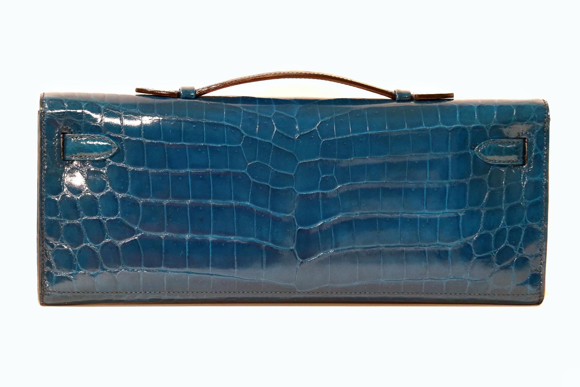 This authentic Hermès Diamond Blue Izmir Crocodile Kelly Cut Clutch is in pristine condition.  Hand crafted by skilled artisans; the Kelly Cut is extremely rare in exotic Niloticus crocodile skin with 18 karat gold diamond hardware.  
Niloticus