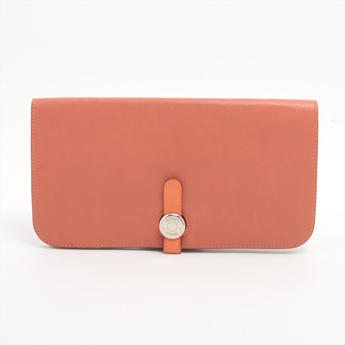 Die Hermès Dogon GM Long Wallet aus orangefarbenem Taurillon Clémence-Leder ist ein raffiniertes Accessoire, das Eleganz mit Alltagsfunktionalität verbindet. Sie ist aus geschmeidigem, genarbtem Leder gefertigt und mit dem charakteristischen