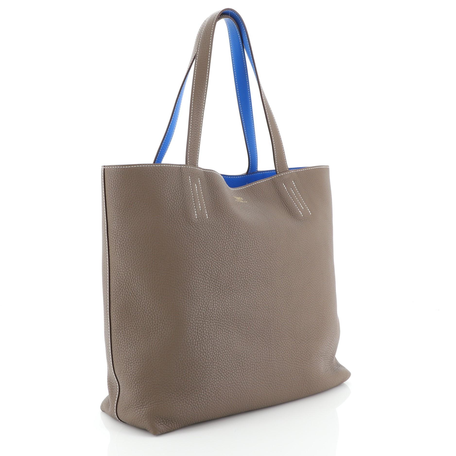 This Hermes Double Sens Tote Clemence 36, crafted from Etoupe neutral Clemence leather, features dual leather straps, all-around contrast stitching, and a stamped Hermes logo. Its wide open top showcases a Bleu Hydra blue Clemence leather interior.