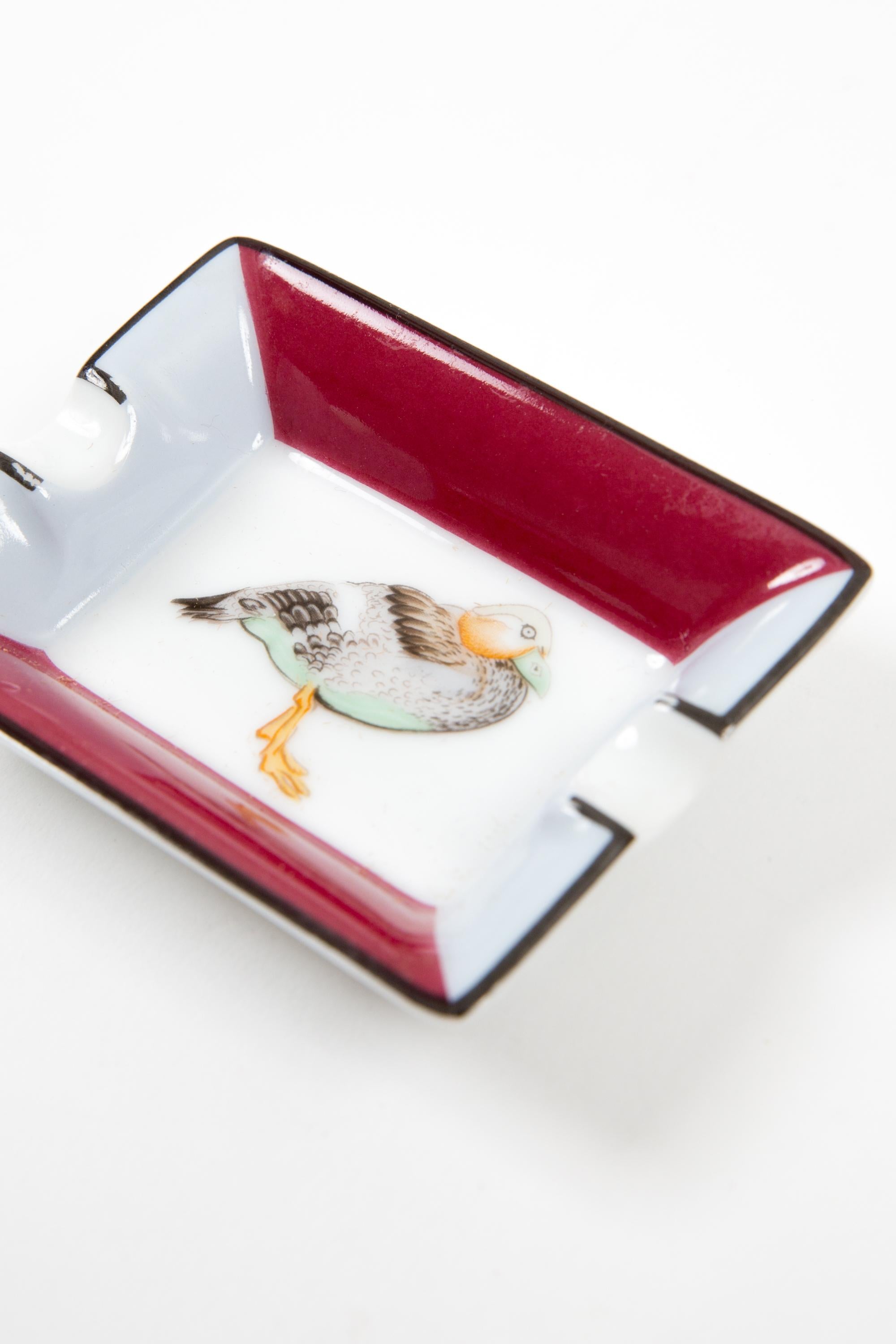 Hermès Multicolor mini “Duck” porcelain de Limoges ashtray organizer featuring a duck motive, a grey and Bordeaux border,  a Hermes gold-tone side signature. 
Circa 1980s 
In good vintage condition. 
Maxi Length 2.9in (7.5cm)
Maxi width 2.3in.