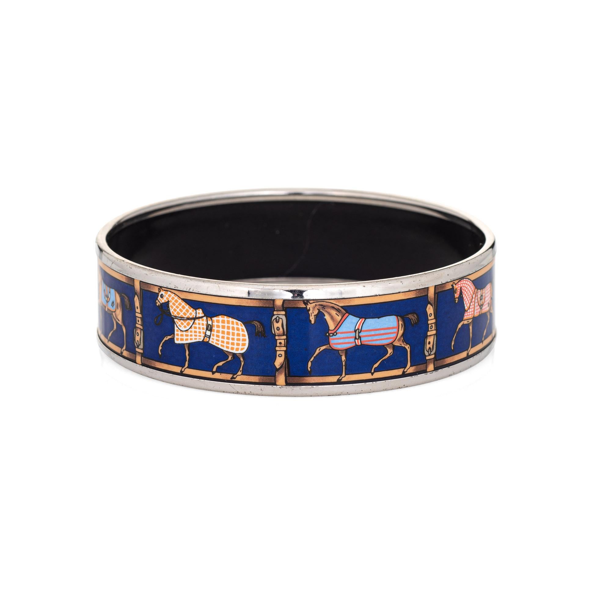 Overview:

Pre-owned vintage Hermes enamel bracelet with a prancing Horse pattern set against a royal blue backdrop, with palladium plated hardware. The horses feature decorative blankets. 

The wide 0.70