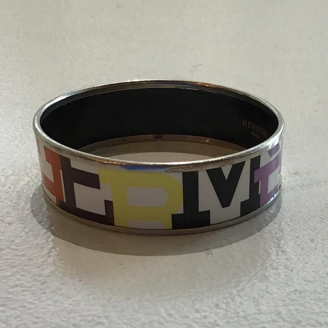 Hermes Enamel Capitales Bangle Bracelet features HERMES spelled out in capital colored letters on white background with silver-tone trim and black enamel interior. On inside “Hermes Paris” “Made in Austria + L”. Designer size 70. Slight wear on