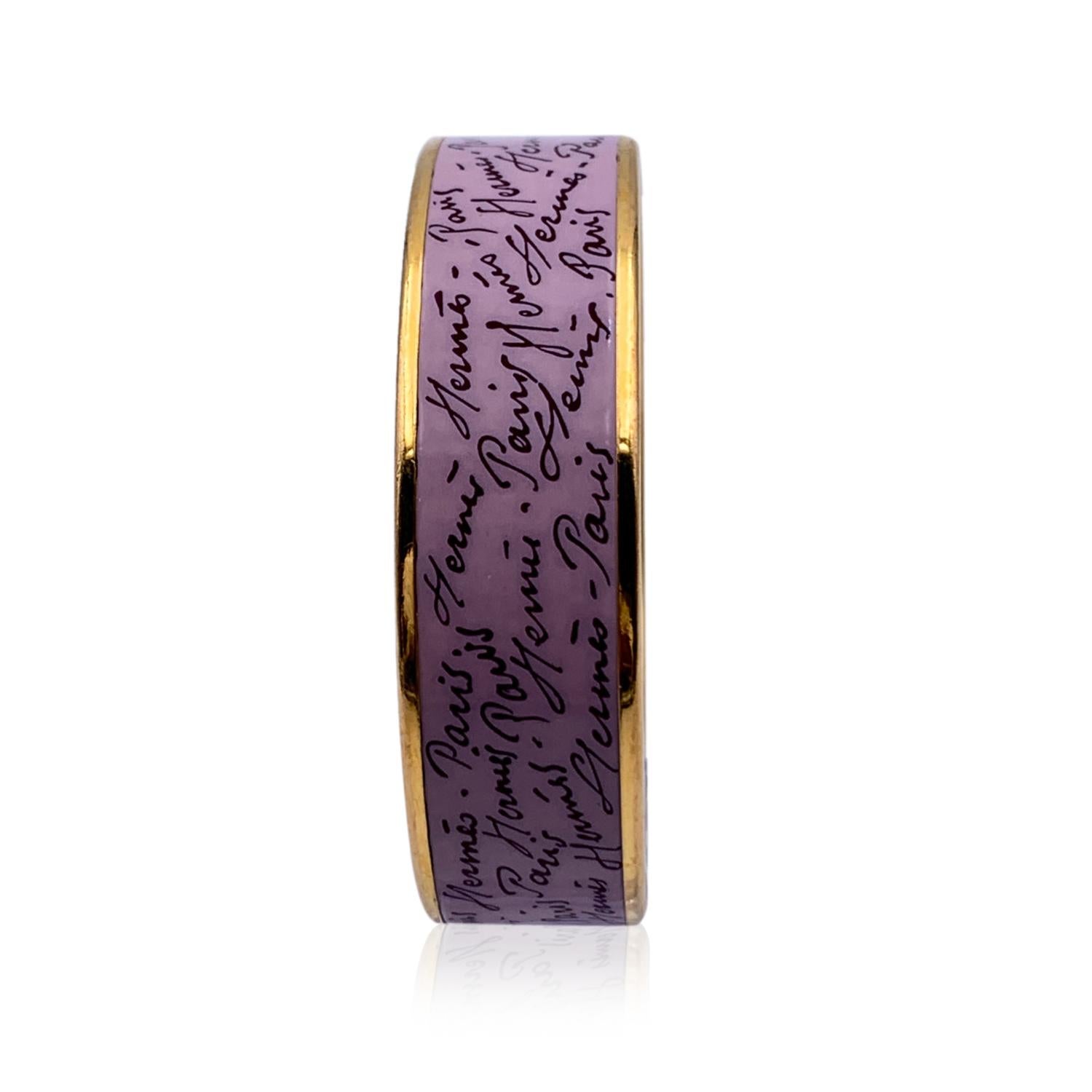 A truly stunning enameled 'Script' bangle bracelet by HERMES. Lilac color with 'Hermes Paris' script print. Gold metal rim. Black enameled interior. Inner diameter: approx. 2.5 inches -' 6.4 cm. HERMES Paris' & 'Made in Austria' embossed inside the