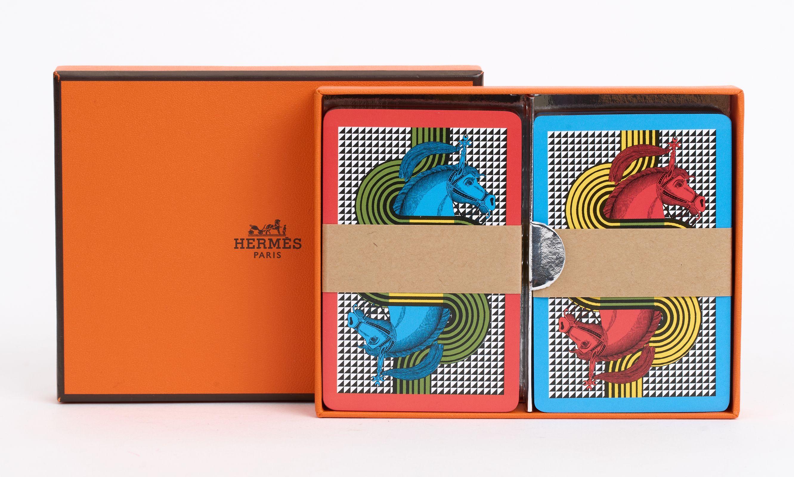 This Hermès Equestre Playing Cards Set contains two decks of bridge playing cards with 54 cards in each. The cards features silver-edges and multi color print. Brand new in original box.