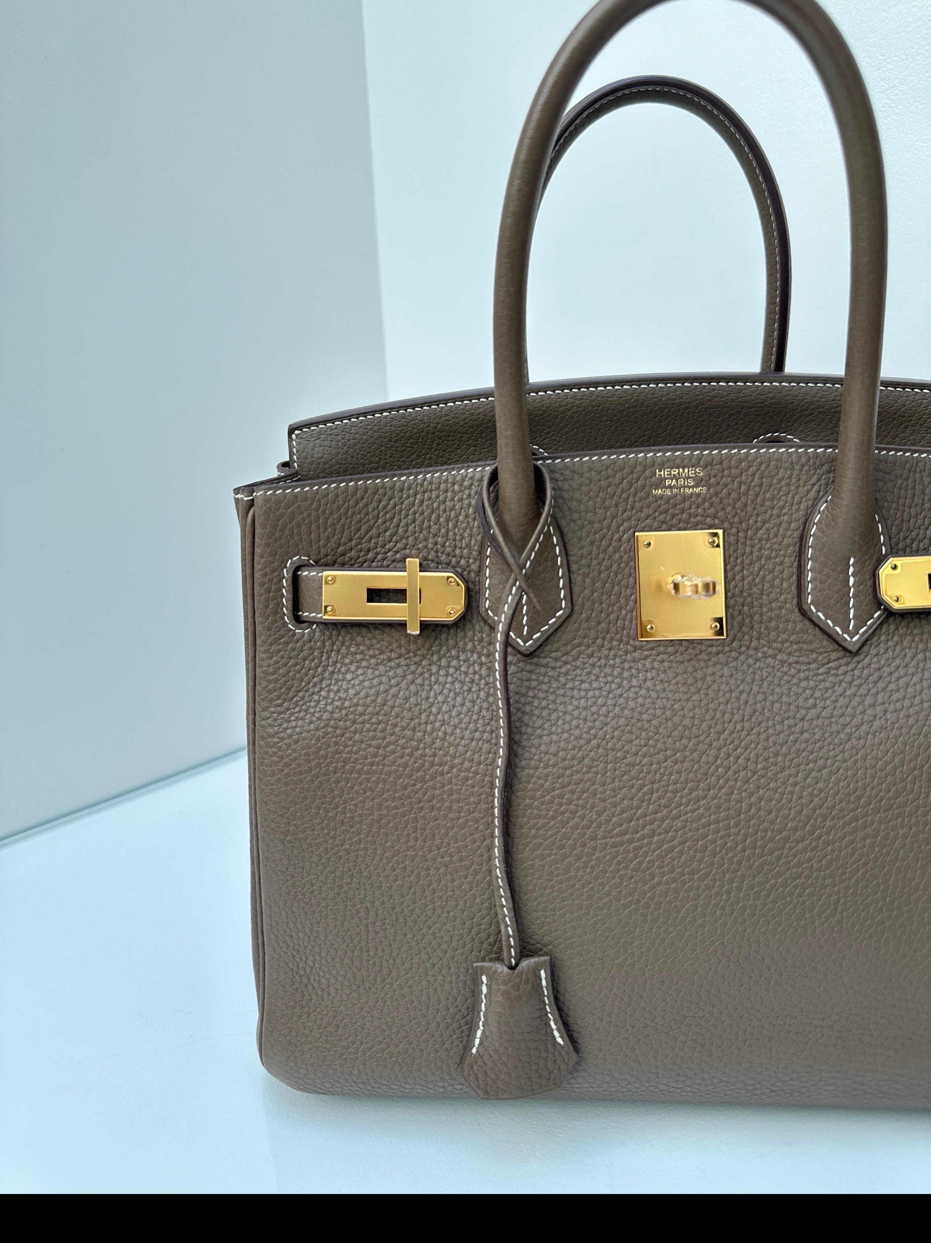 Sac Hermès Etoupe Birkin 30. Excellent état. Plastique encore sur le matériel. Matériel doré. Intérieur propre. Couleur neutre et taille 30 les plus recherchées. Comprend une clochette, un cadenas, des clés et un sac à poussière. Garantie