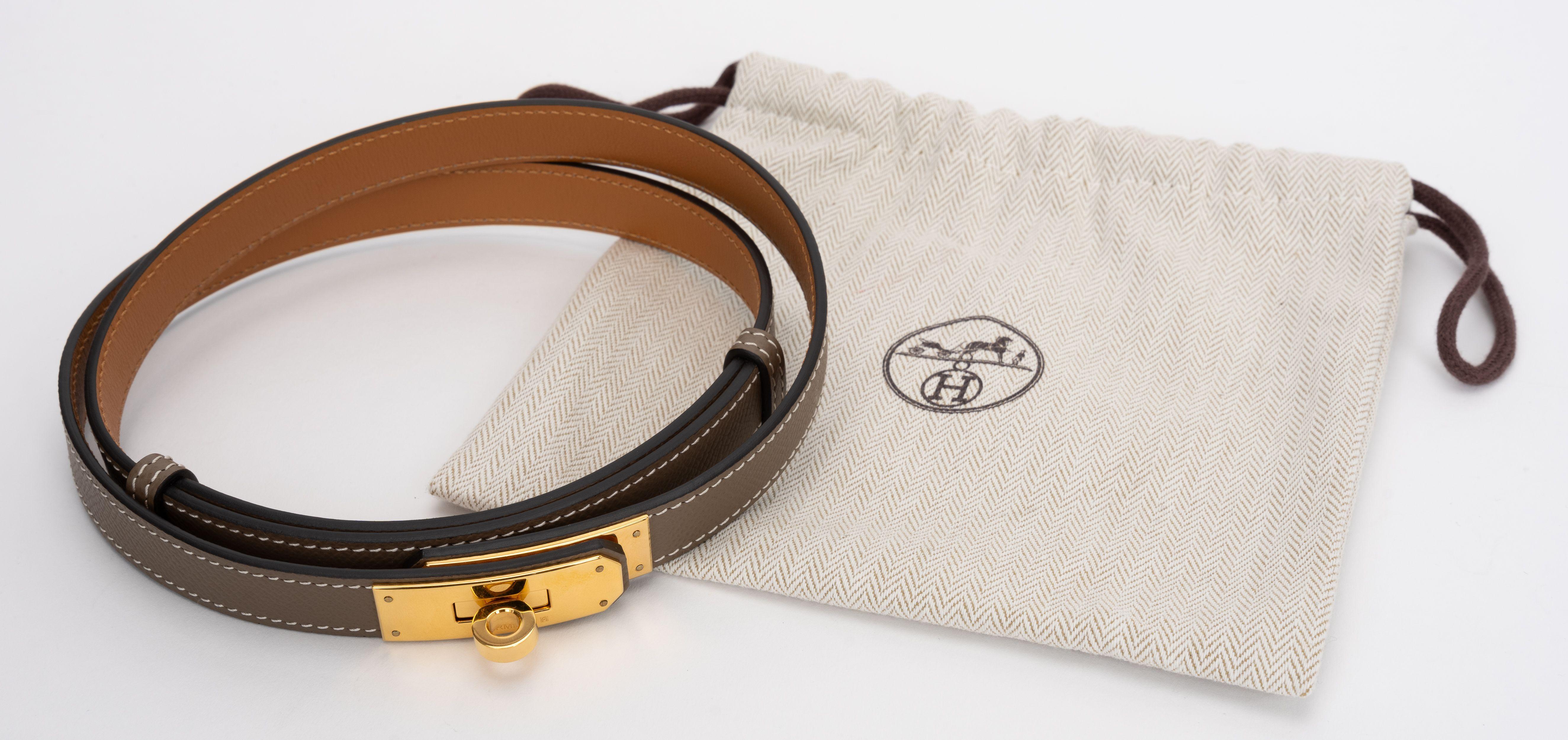 La ceinture Kelly Epsom d'Hermes est en cuir d'epsom etoupe, avec un cadenas Kelly doré sur le devant. La ceinture peut être portée aussi bien à la taille qu'en bas de la taille. Largeur : 0,71