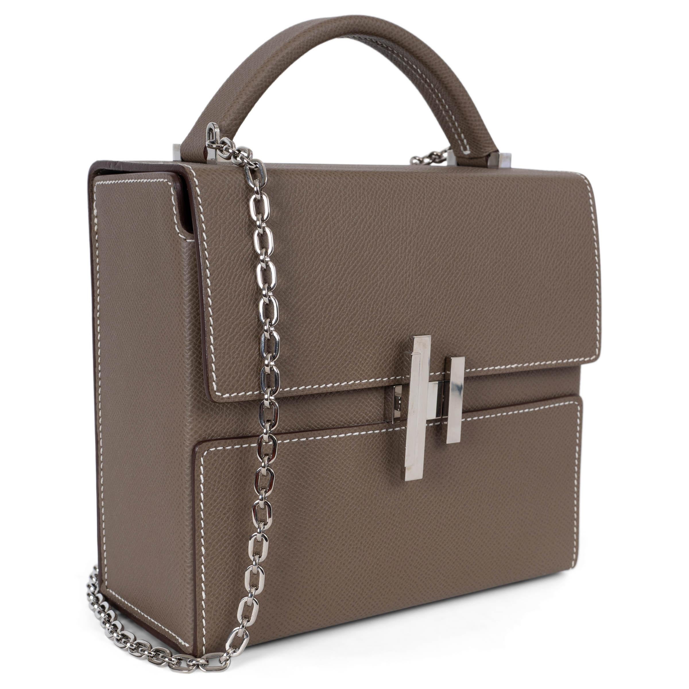 This 100% authentic Hermès Cinhetic 18 bag in Etoupe (taupe) Veau Epsom leather is a statement of modern elegance. Accented with contrasting white stitching and palladium hardware, its structured box shape is complemented by a refined top handle and