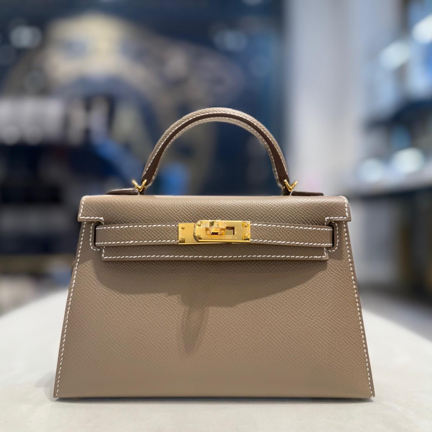 Jewels Aficionado offers this Hermès Mini Kelly in Etoupe Epsom leather, a compact yet luxurious icon of timeless sophistication. The signature Etoupe hue—a refined beige with subtle taupe undertones—is enhanced by contrasting white stitching,