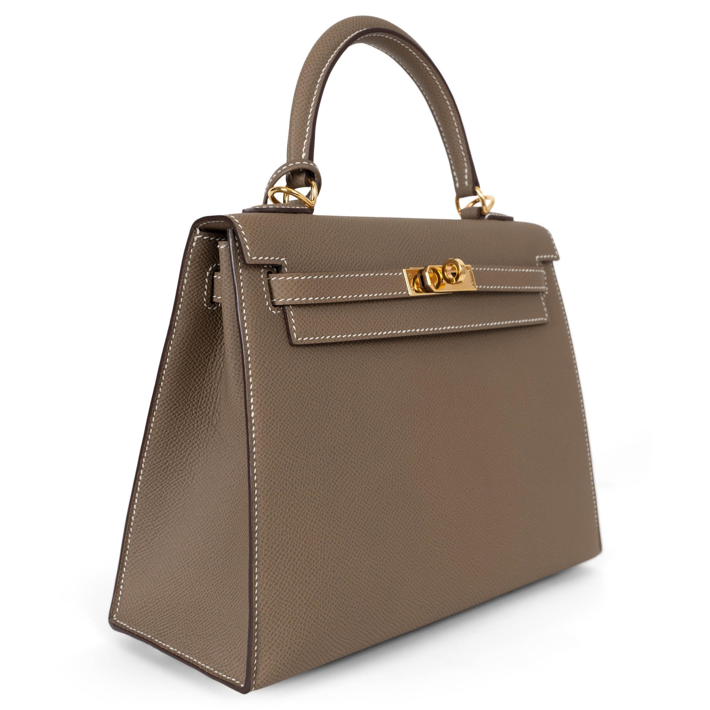 This 100% authentic Hermès Kelly 25 Sellier bag in Etoupe (taupe) Veau Epsom leather is a timeless classic. Featuring elegant contrasting white stitching and gold-plated hardware, it embodies sophistication and understated luxury. The structured