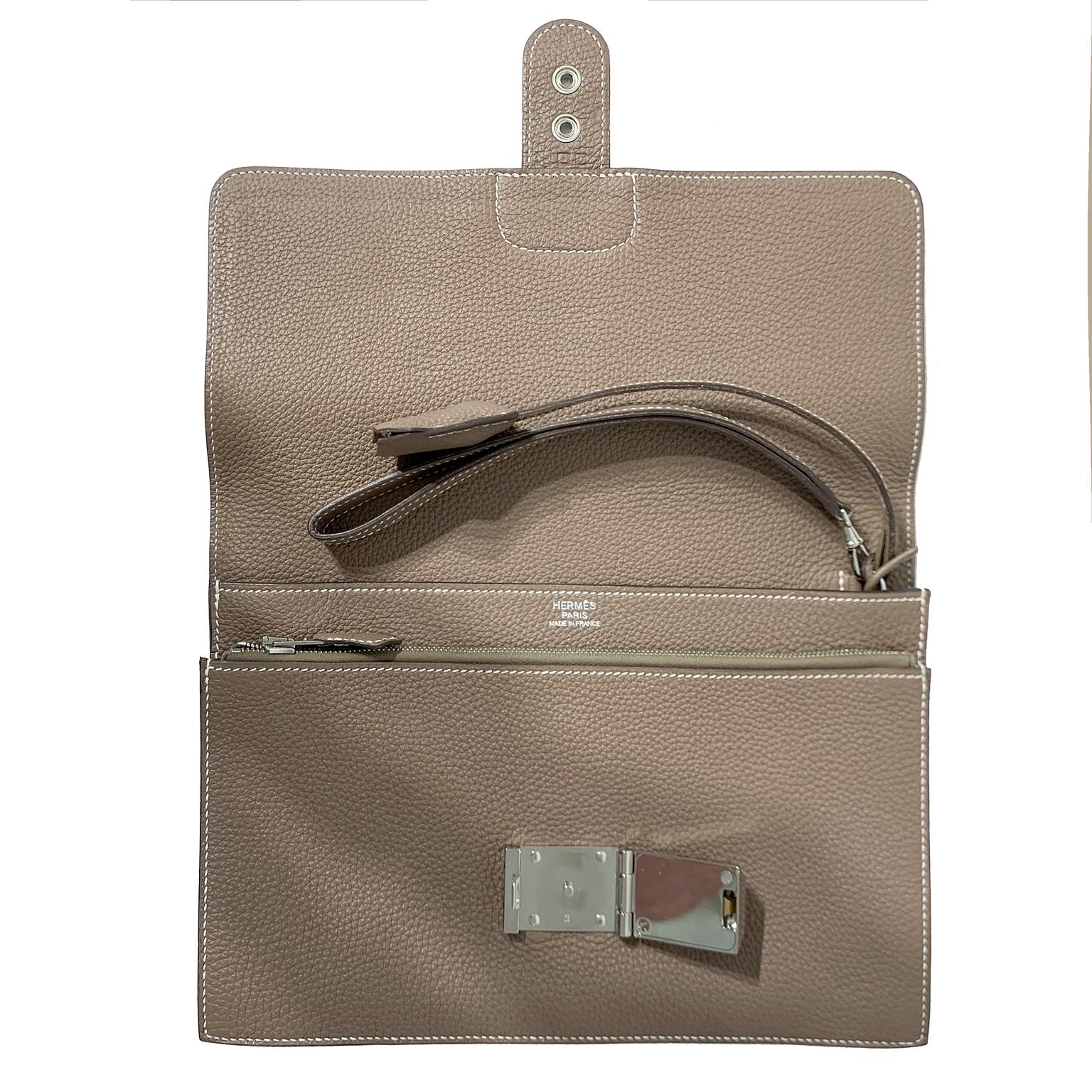 This authentic Hermès Etoupe Togo Jet Clutch is in pristine condition.  Elegant and timeless, the Jet is a unisex style that easily carries the essentials with panache.
Neutral greige Etoupe Togo leather is textured and durable, yet soft to the