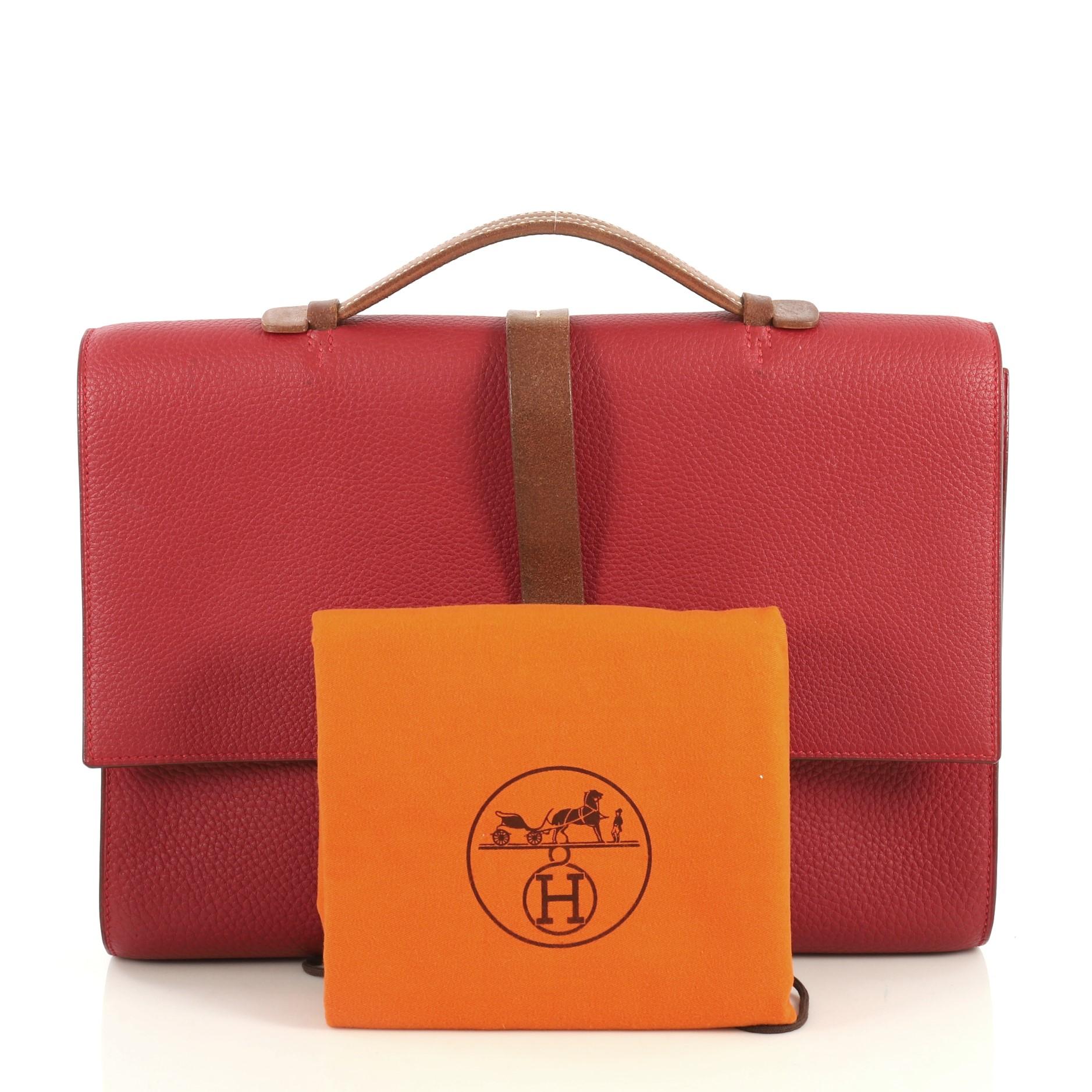 This Hermes Etriviere II Briefcase Fjord 38, crafted in Rouge Vif red Fjord and Fauve leather, features a leather top handle, wrap-around leather strap and palladium hardware. Its buckle closure opens to a Rouge Vif red leather interior. Date stamp
