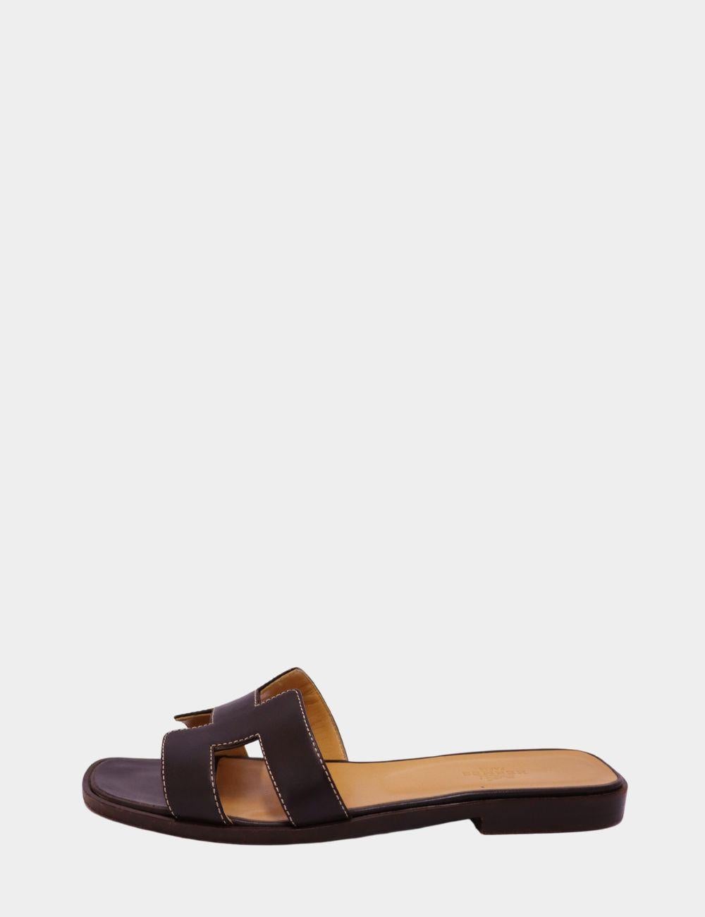 Entrez dans le luxe sans effort avec ces sandales iconiques Hermès Oran en cuir marron riche. Confectionnées en cuir de veau lisse, elles présentent la découpe 