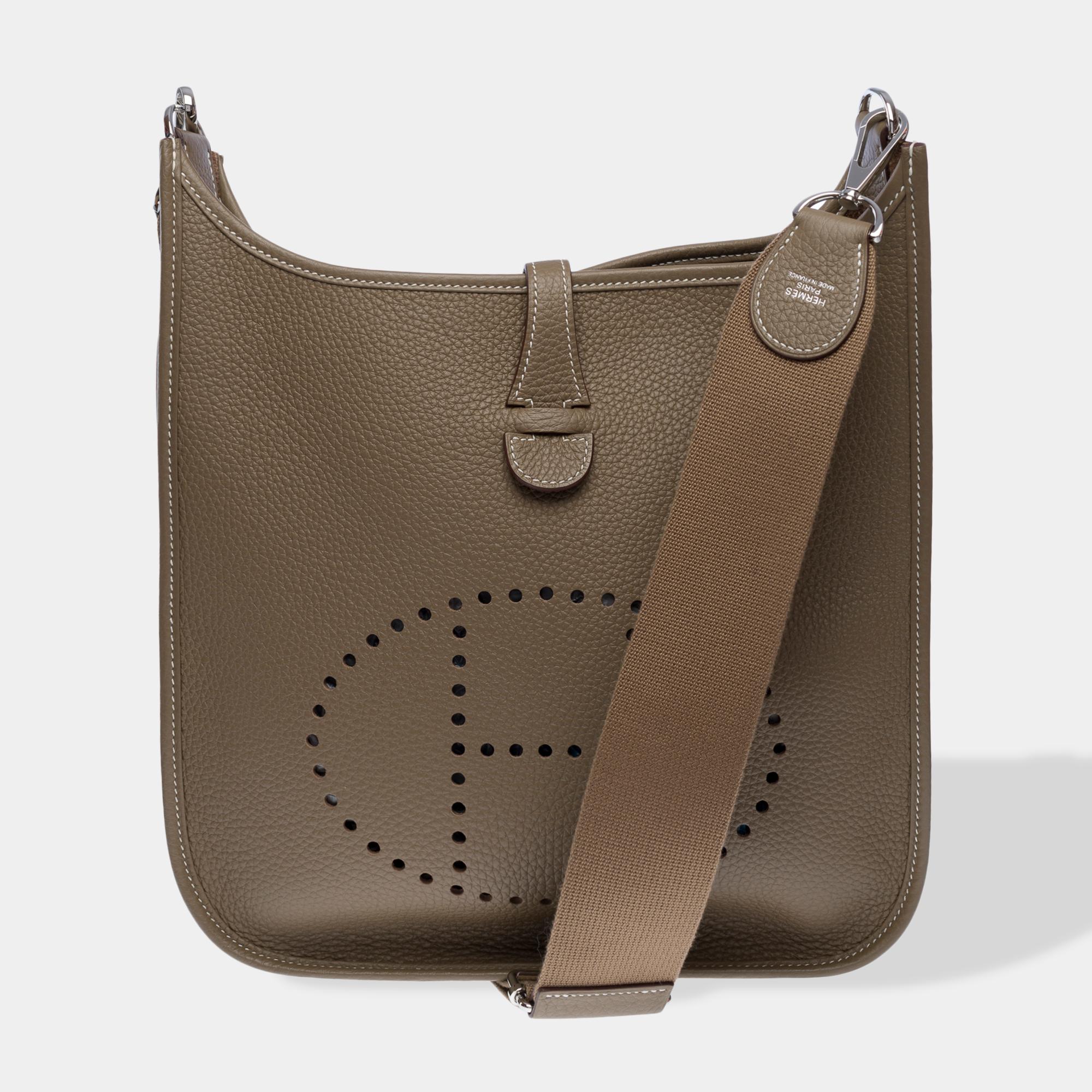 Iconic​ ​Hermes​ ​Evelyne​ ​29​ ​shoulder​ ​bag​ ​in​ ​Etoupe​ ​Togo​ ​calfskin​ ​with​ ​white​ ​stitching,​ ​palladium​ ​silver​ ​metal​ ​trim,​ ​a​ ​removable​ ​gray​ ​canvas​ ​shoulder​ ​strap​ ​allowing​ ​for​ ​shoulder​ ​or​ ​crossbody​