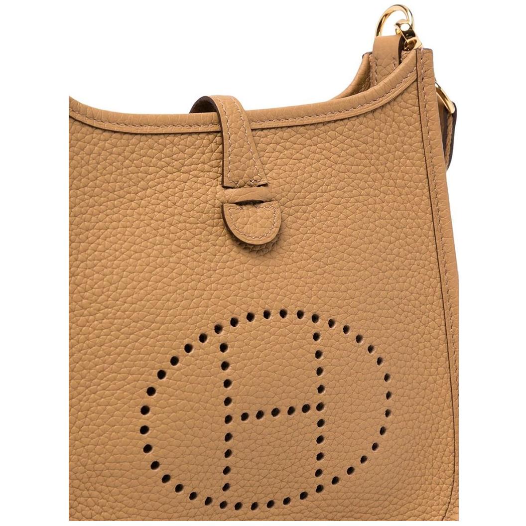 Crafted from an earthy camel-toned leather with gold-tone hardware, this Evelyne bag by Hermès is stylish yet functional, and designed in a traditional saddle-like shape with a perforated 'H' logo decorating the front. Featuring an adjustable