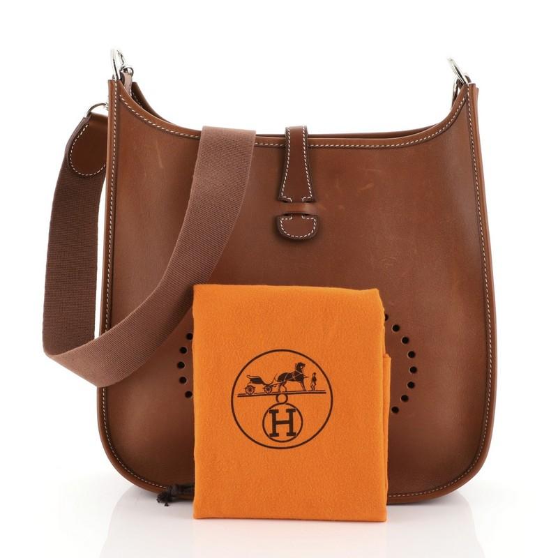 This Hermes Evelyne Crossbody Gen I Box Calf PM, crafted from Fauve brown Barenia leather, features a signature perforated H design at the front, adjustable textile shoulder strap and palladium hardware. It opens to a brown raw leather interior.