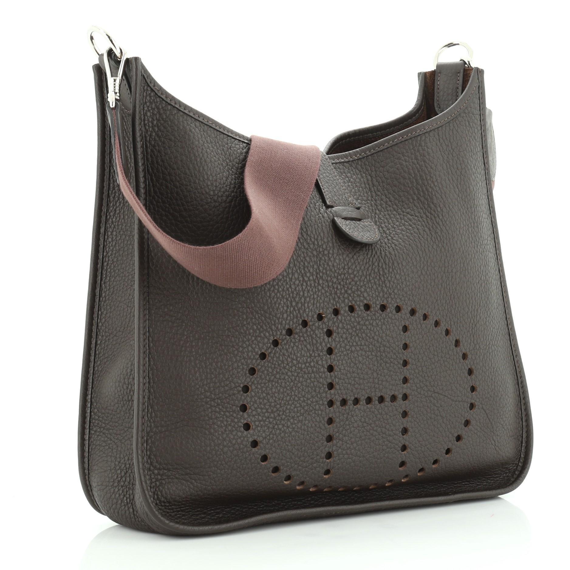 This Hermes Evelyne Crossbody Gen I Clemence GM is an everyday bag that was originally designed to hold horse grooming equipment. Crafted in Ebene brown Clemence leather, features perforated H design at the front, textile shoulder strap, and