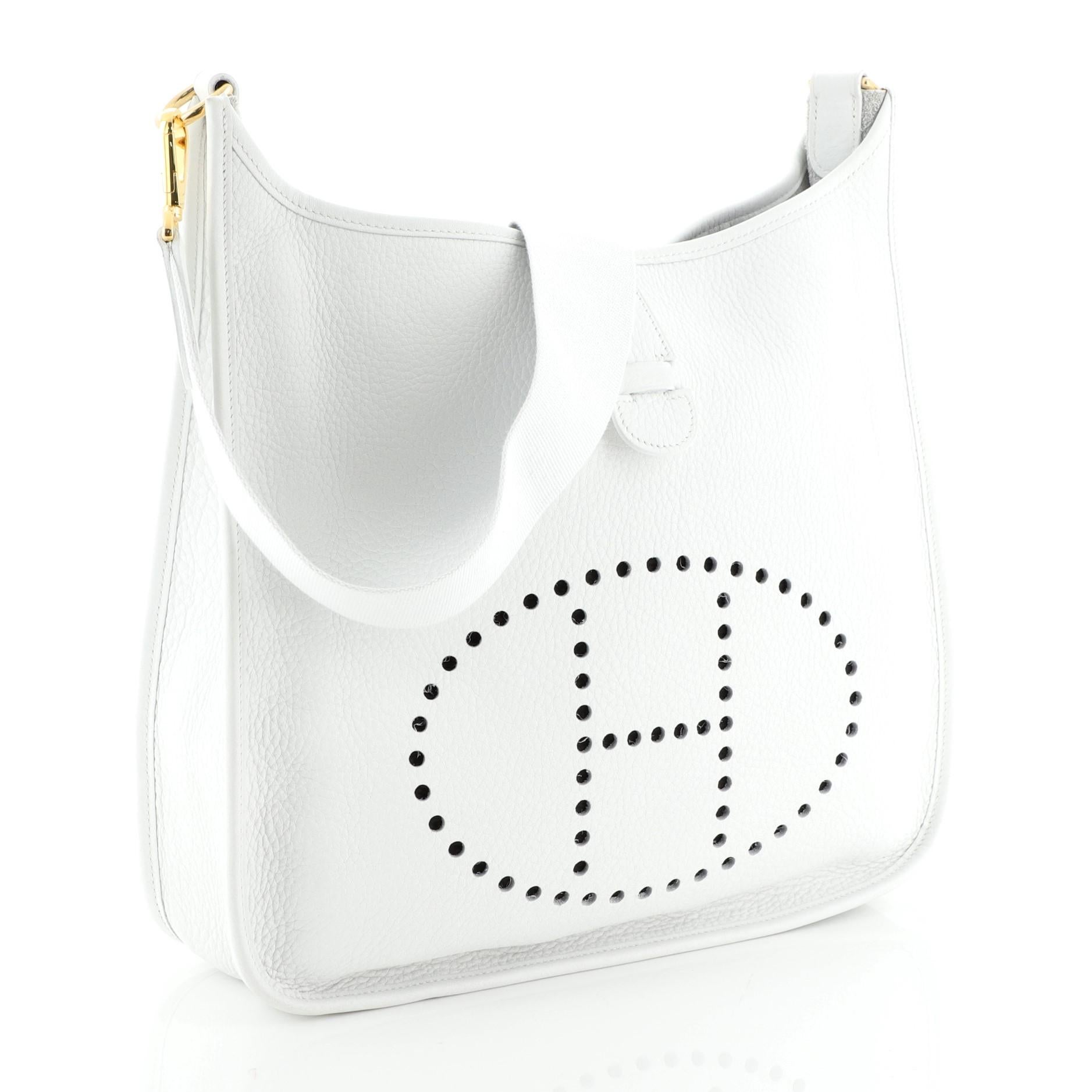 This Hermes Evelyne Crossbody Gen I Clemence GM, crafted in Blanc white Clemence leather, features perforated H design at the front, textile shoulder strap, and gold hardware. It opens to a gray raw leather interior. Date stamp reads: F Square