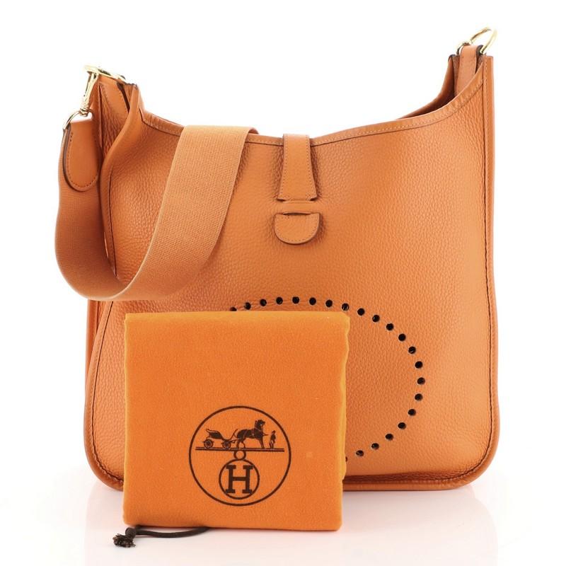 This Hermes Evelyne Crossbody Gen I Togo PM, crafted in Orange H orange Togo leather, features long canvas strap, perforated H design at the front, and gold hardware. Its frontal leather tab closure opens to an Orange H orange leather interior. Date