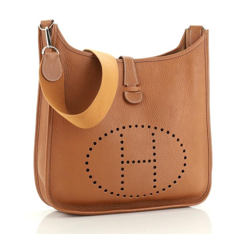 This Hermes Evelyne Crossbody Gen II Clemence GM, crafted in Gold brown Clemence leather, features signature perforated H design at the front, long crossbody strap, and palladium hardware. It opens to a Gold brown raw leather interior. Date stamp