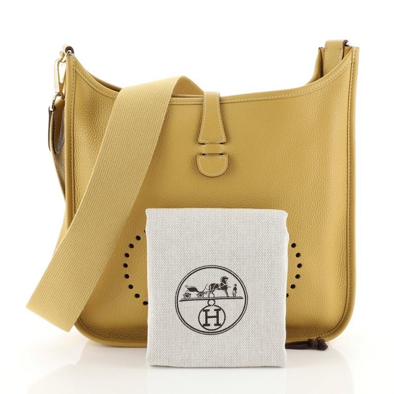 This Hermes Evelyne Crossbody Gen II Clemence PM, crafted in Curry yellow Clemence leather, features a long crossbody strap, perforated H design at the front, and gold hardware. Its top leather tab closure opens to a Curry yellow raw leather