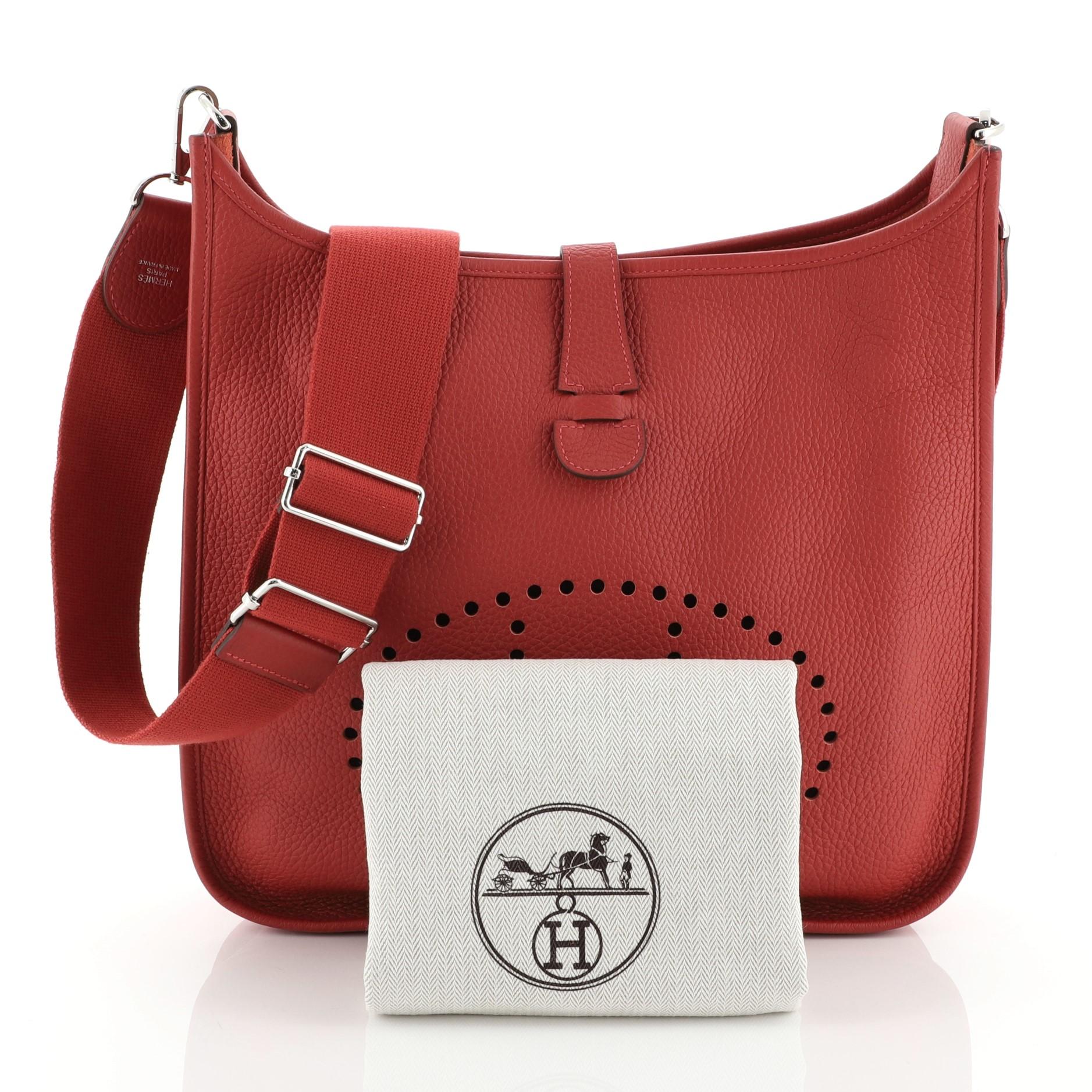 This Hermes Evelyne Crossbody Gen III Clemence GM, crafted in Rouge Vif red Clemence leather, features perforated H design at the front, accessible back pocket, adjustable shoulder strap, and palladium hardware. It opens to a Rouge Vif red raw