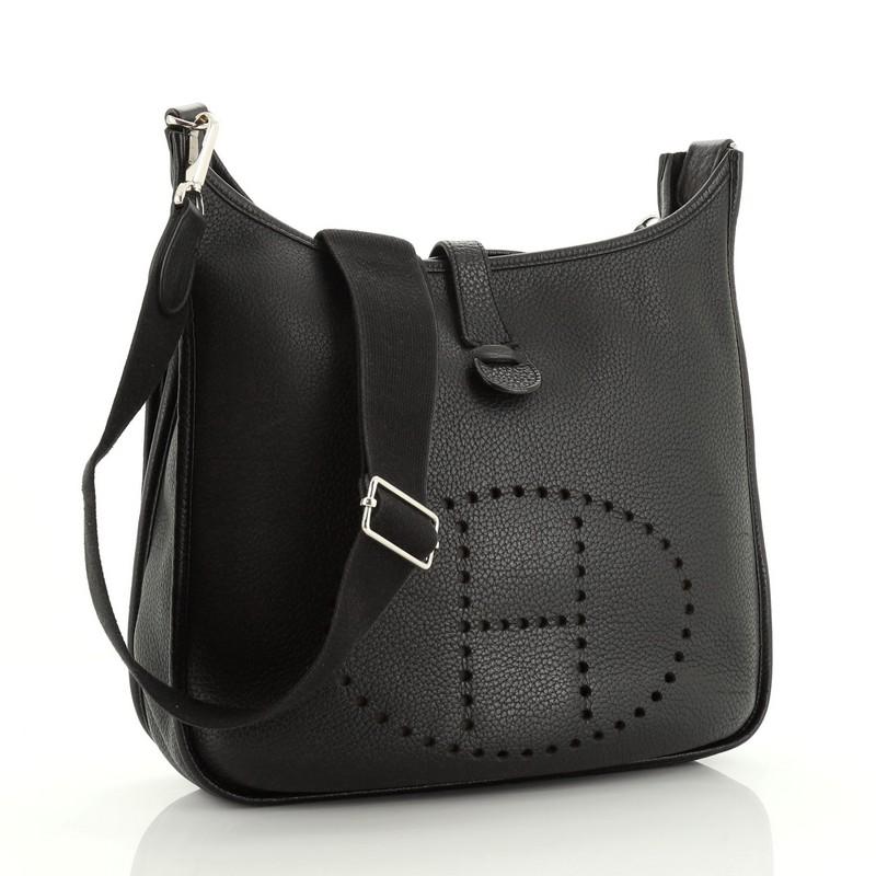 This Hermes Evelyne Crossbody Gen III Clemence GM, crafted in Noir black Clemence leather, features perforated H design at the front, accessible back pocket, adjustable shoulder strap, and palladium hardware. It opens to a Noir black raw leather