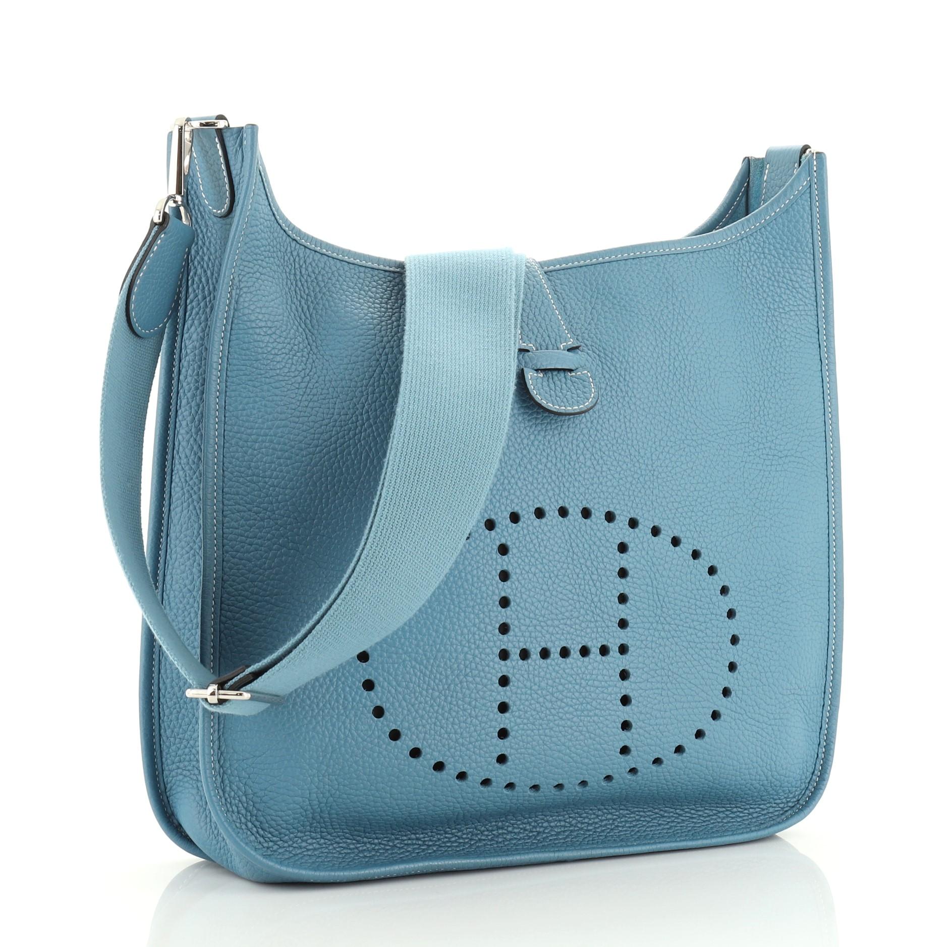 This Hermes Evelyne Crossbody Gen III Clemence GM, crafted in Bleu Jean blue Clemence leather, features perforated H design at the front, accessible back pocket, adjustable shoulder strap, and palladium hardware. It opens to a Bleu Jean blue raw