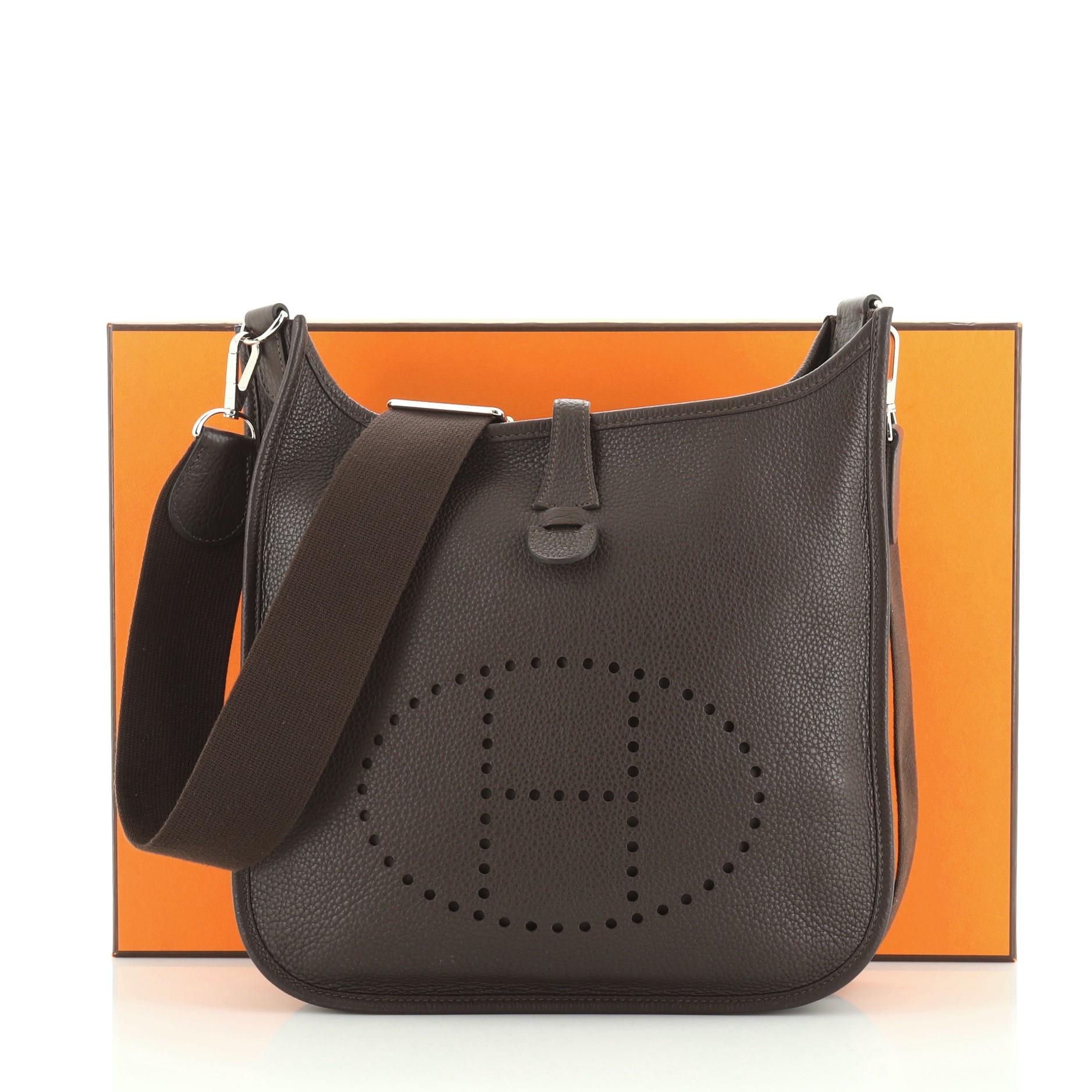 This Hermes Evelyne Crossbody Gen III Clemence PM, crafted in Ebene brown Clemence leather, features perforated H design at the front, accessible back pocket, adjustable textile shoulder strap, and palladium hardware. It opens to an Ebene brown raw