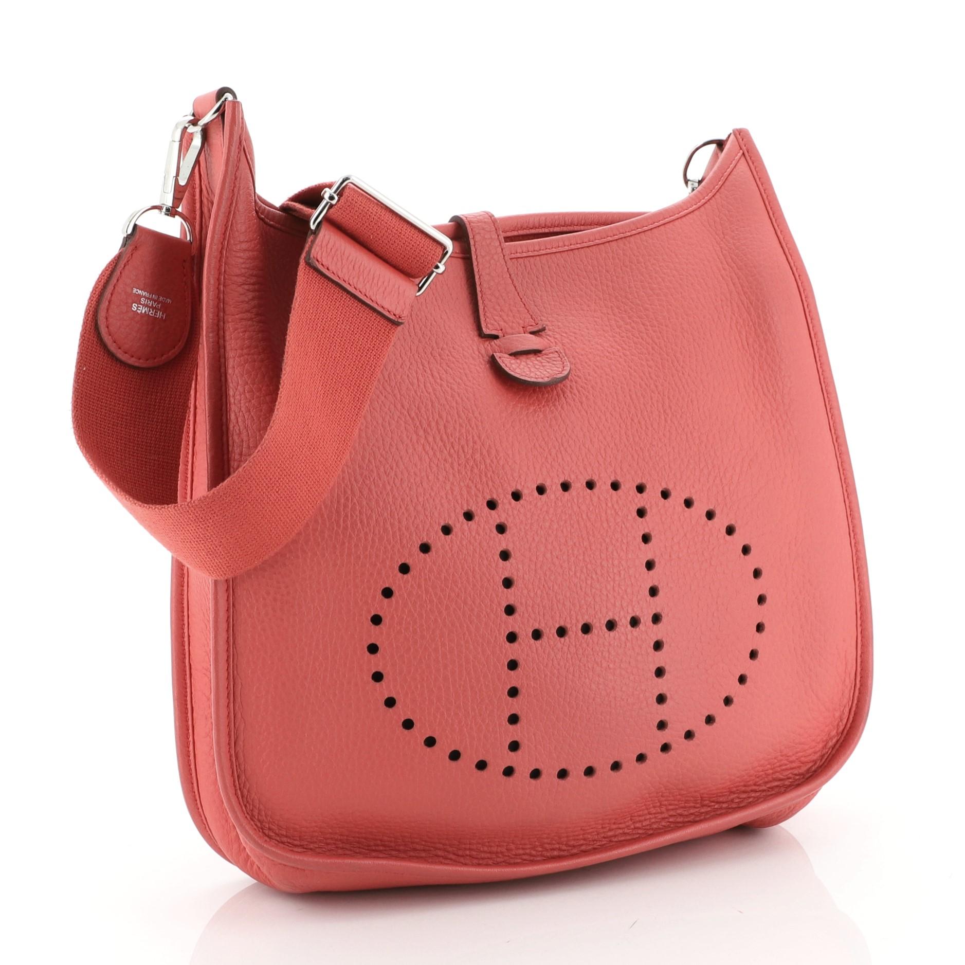 This Hermes Evelyne Crossbody Gen III Clemence PM, crafted in Bougainvillier Clemence leather, features perforated H design at the front, accessible back pocket, textile shoulder strap, and palladium hardware. It opens to a Bougainvillier raw